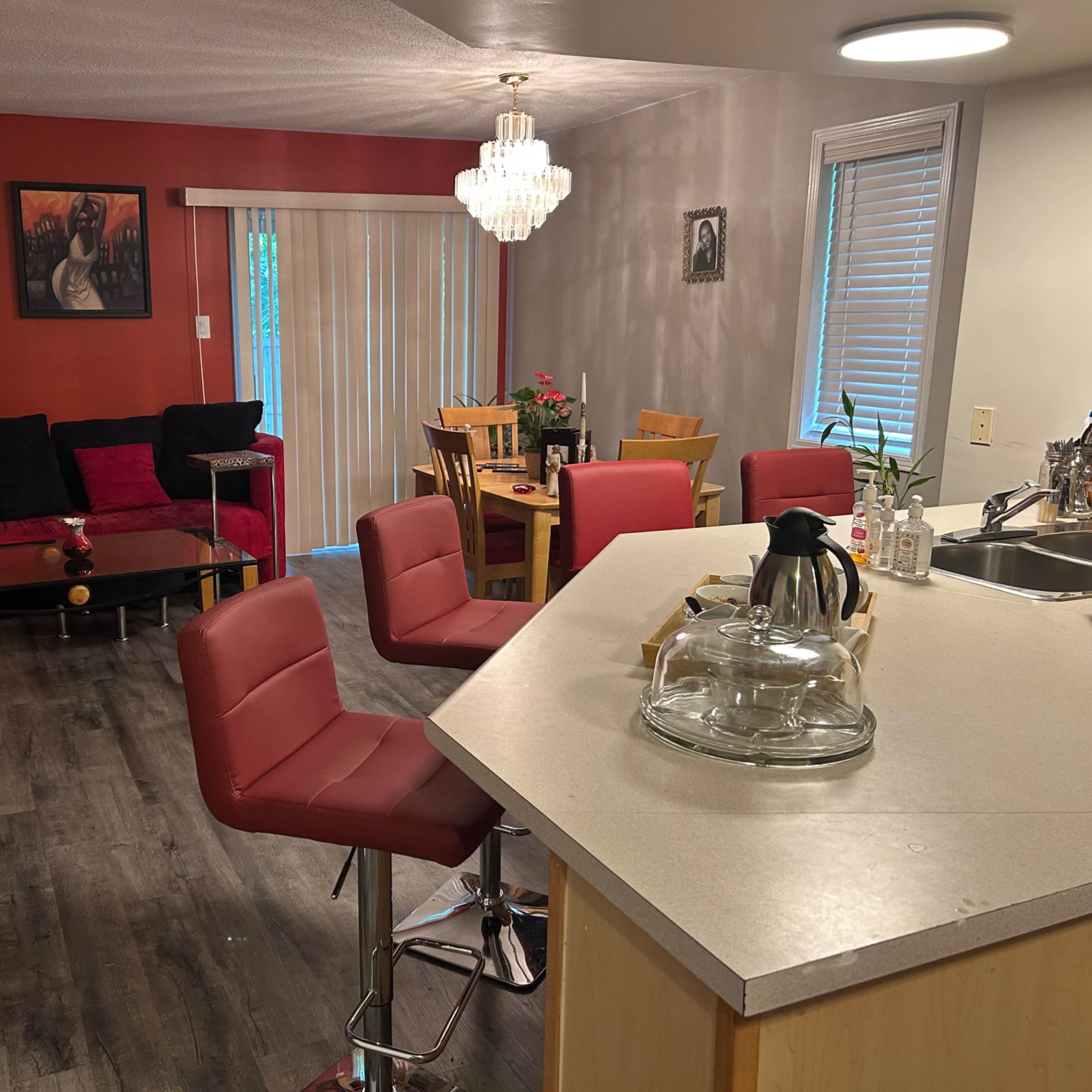 A cozy living area and kitchen with a modern layout, featuring red and neutral tones, seating arrangements, and a dining table.