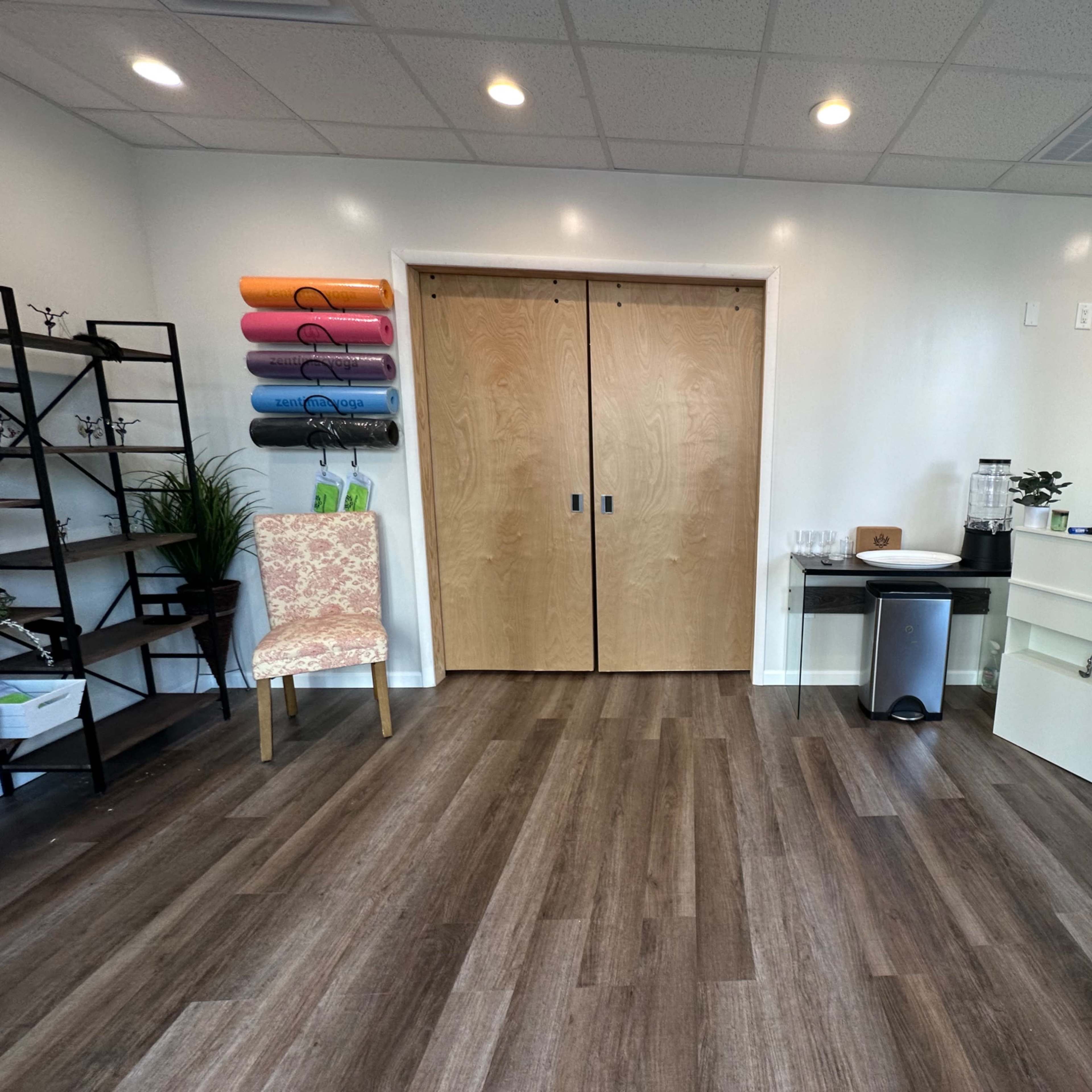 A bright, modern office space with a reception area featuring a desk, a chair, and colorful yoga mats on a shelf.