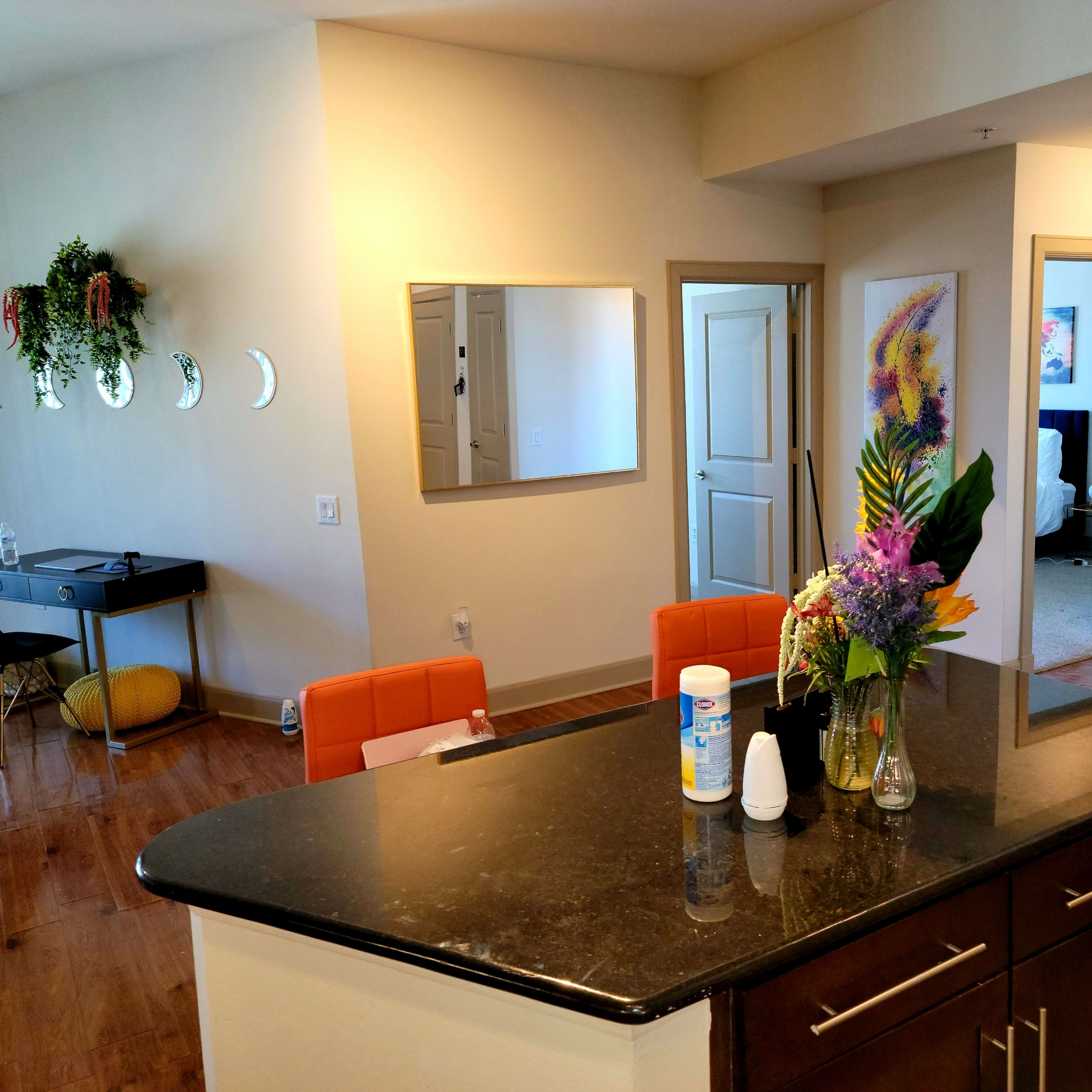 A modern kitchen area features a dark countertop with a vase of flowers, orange chairs, and doorways leading to other rooms.
