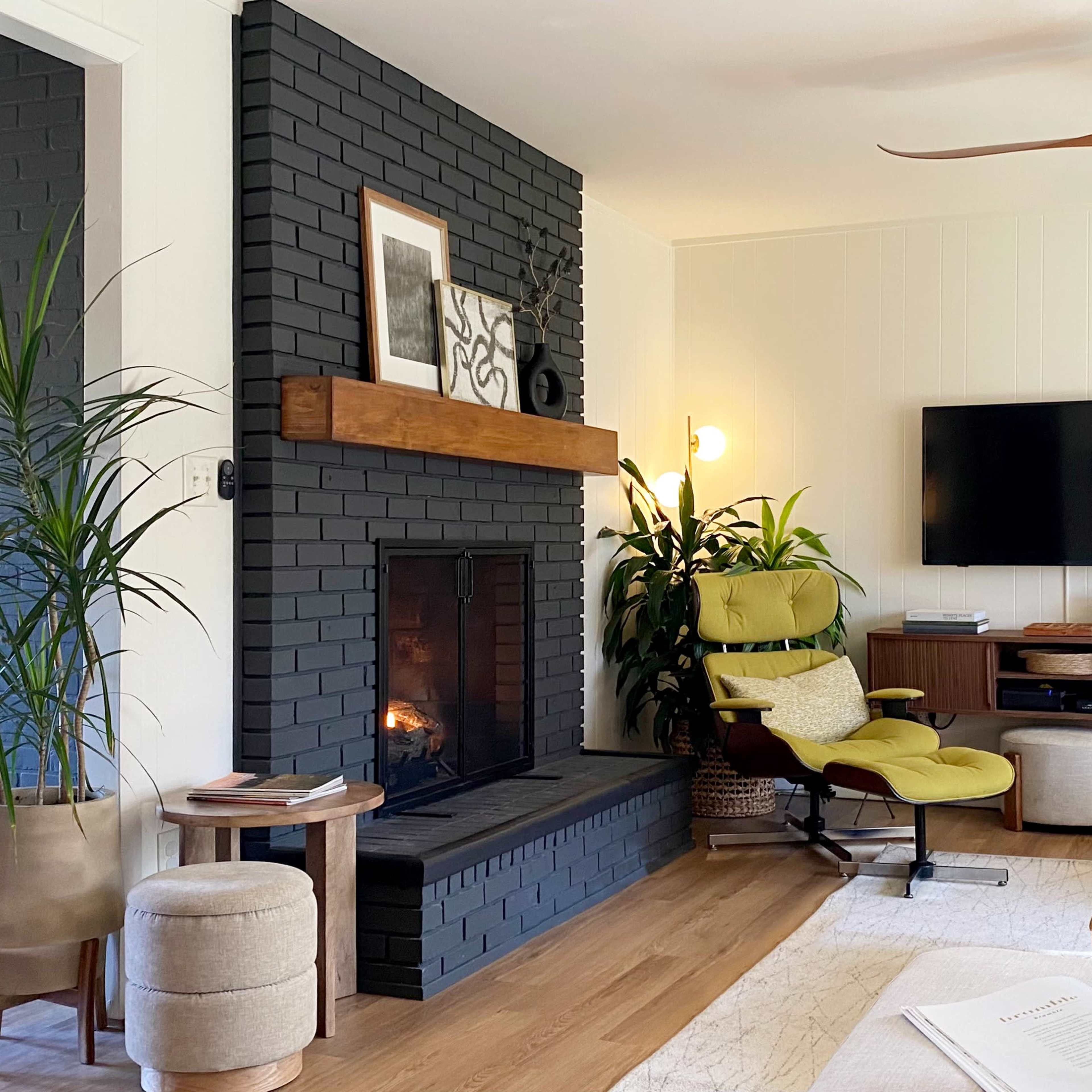 The living room features a dark brick fireplace, a mounted television, a green accent chair, and various indoor plants.