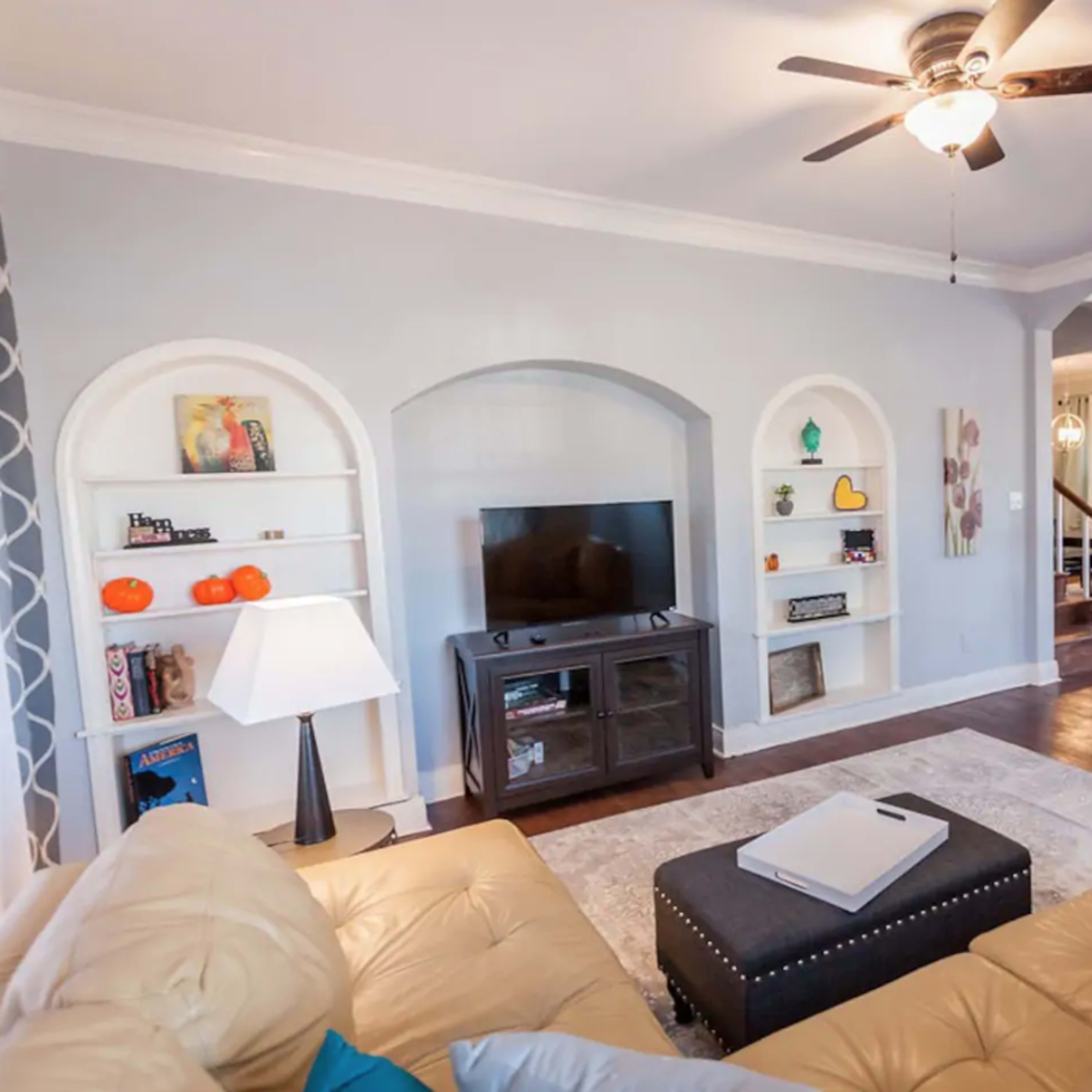 The scene features a living room with a beige sectional sofa, a brick fireplace, built-in bookshelves, and a television on a stand.