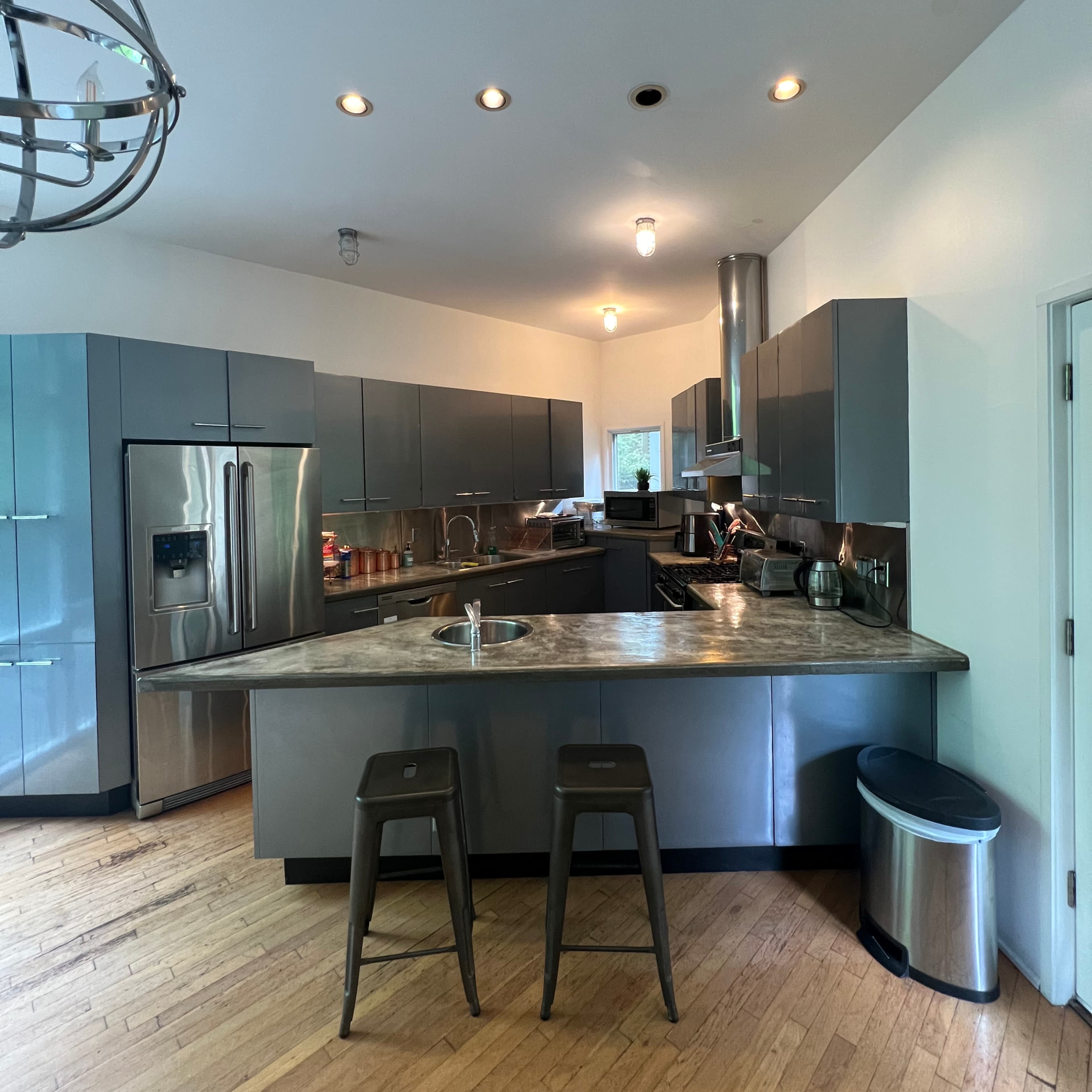 A modern kitchen features stainless steel appliances, a large island with seating, and hardwood flooring.