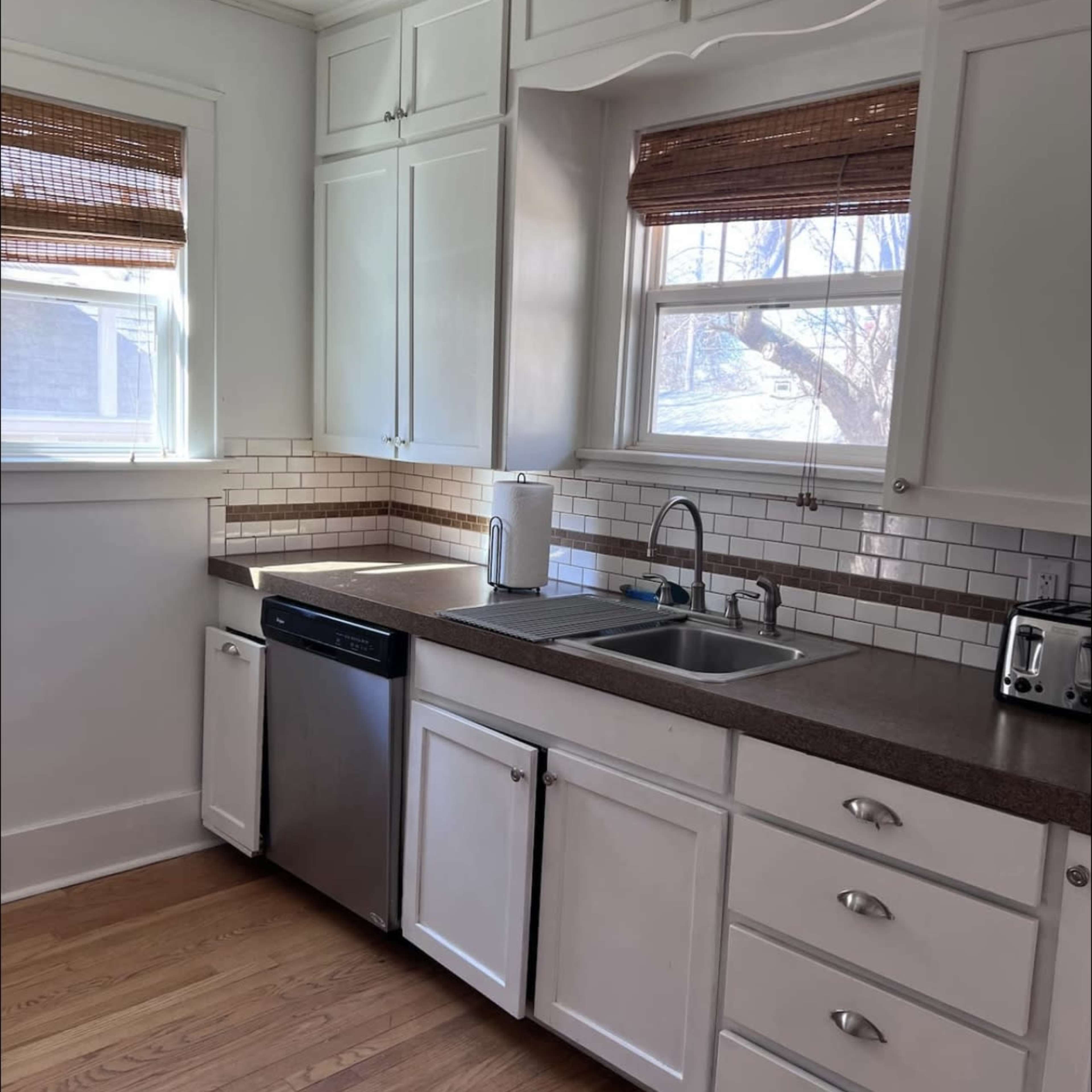 A kitchen with white cabinetry, a stainless steel dishwasher, a double sink, and a countertop with light brown accents.
