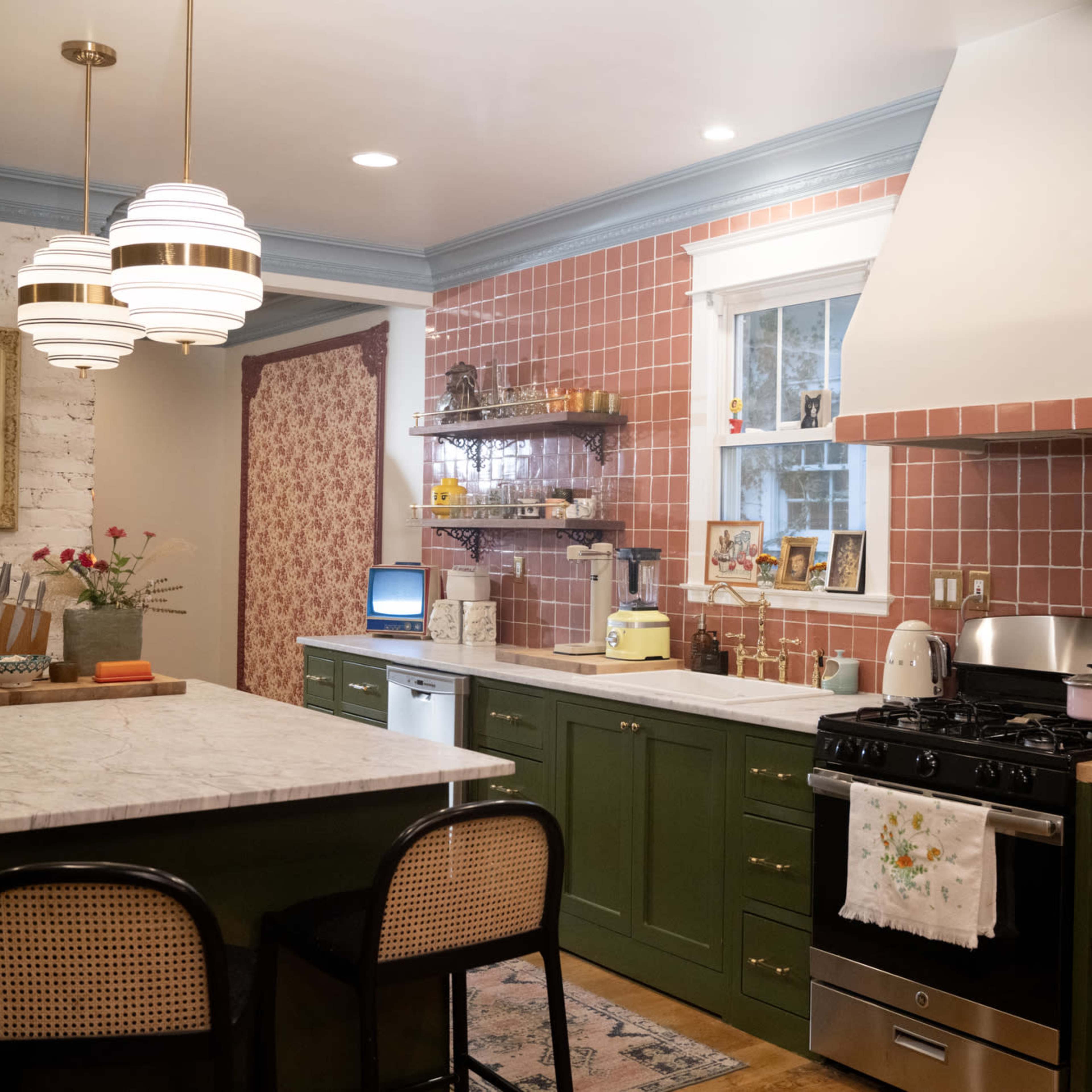 A modern kitchen featuring a marble island, green cabinetry, pink tiled walls, and vintage decor elements.