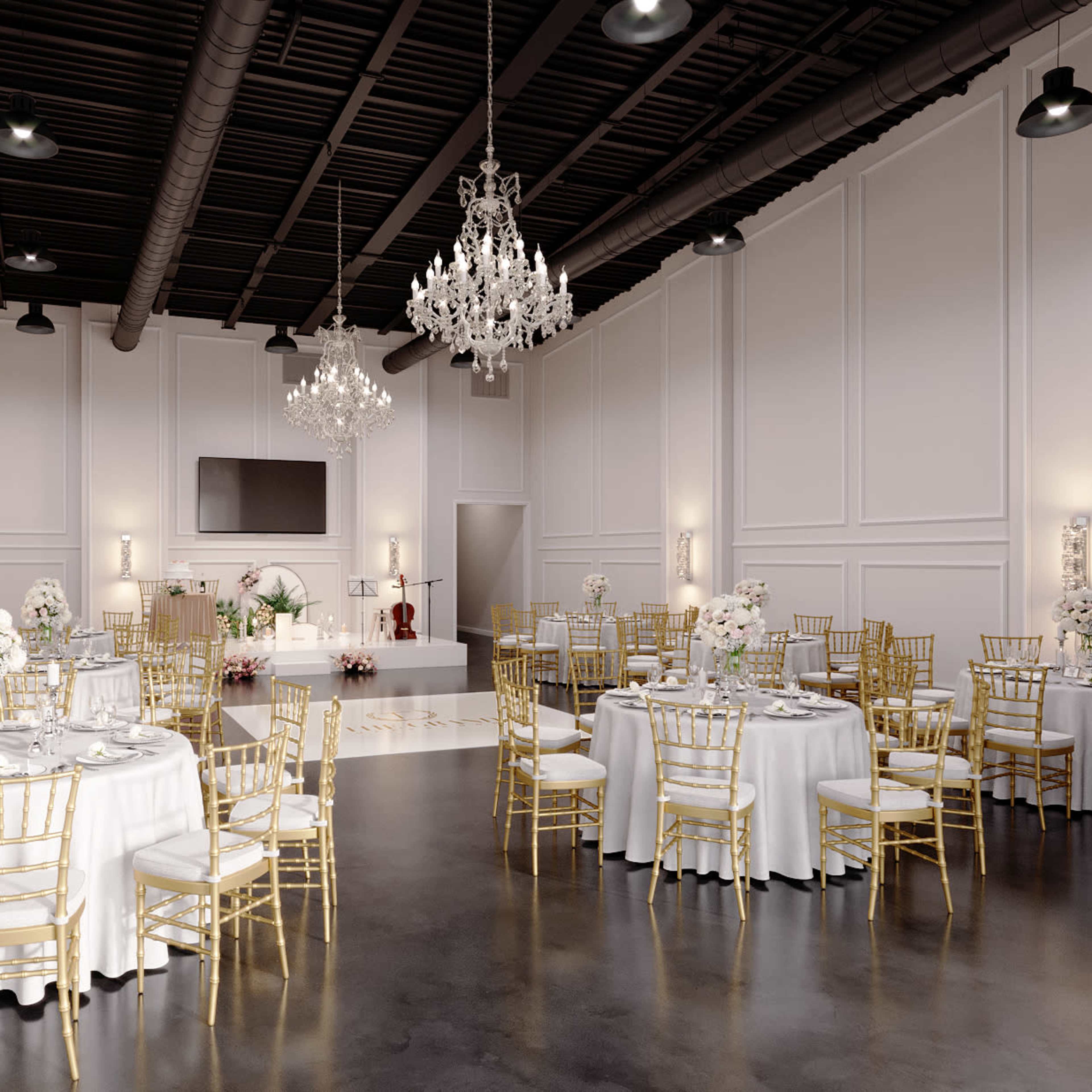 A spacious event hall features round dining tables with white tablecloths and golden chairs, illuminated by chandeliers and flanked by elegant decor.