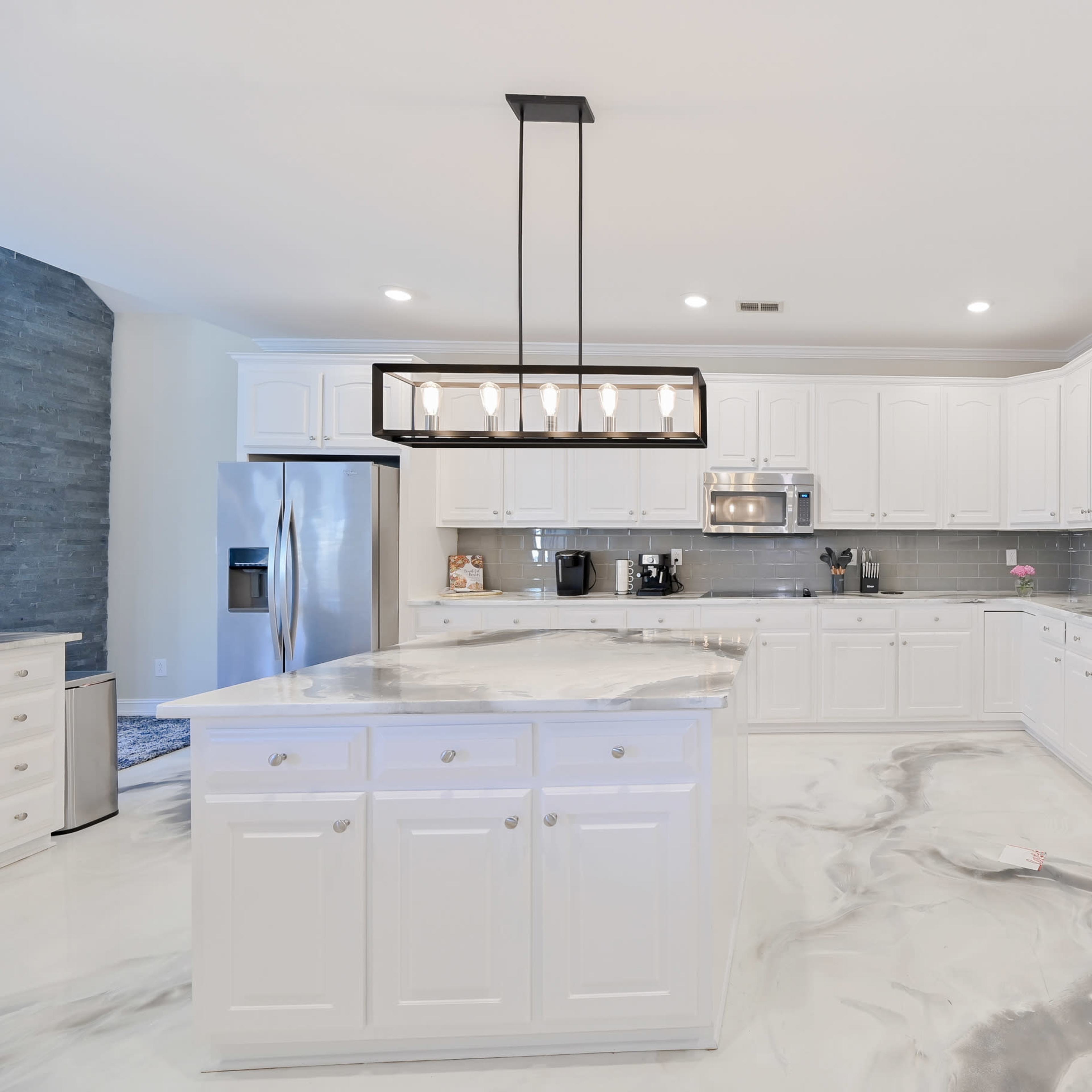 The kitchen features white cabinetry, stainless steel appliances, and a large island with a marble-patterned countertop.