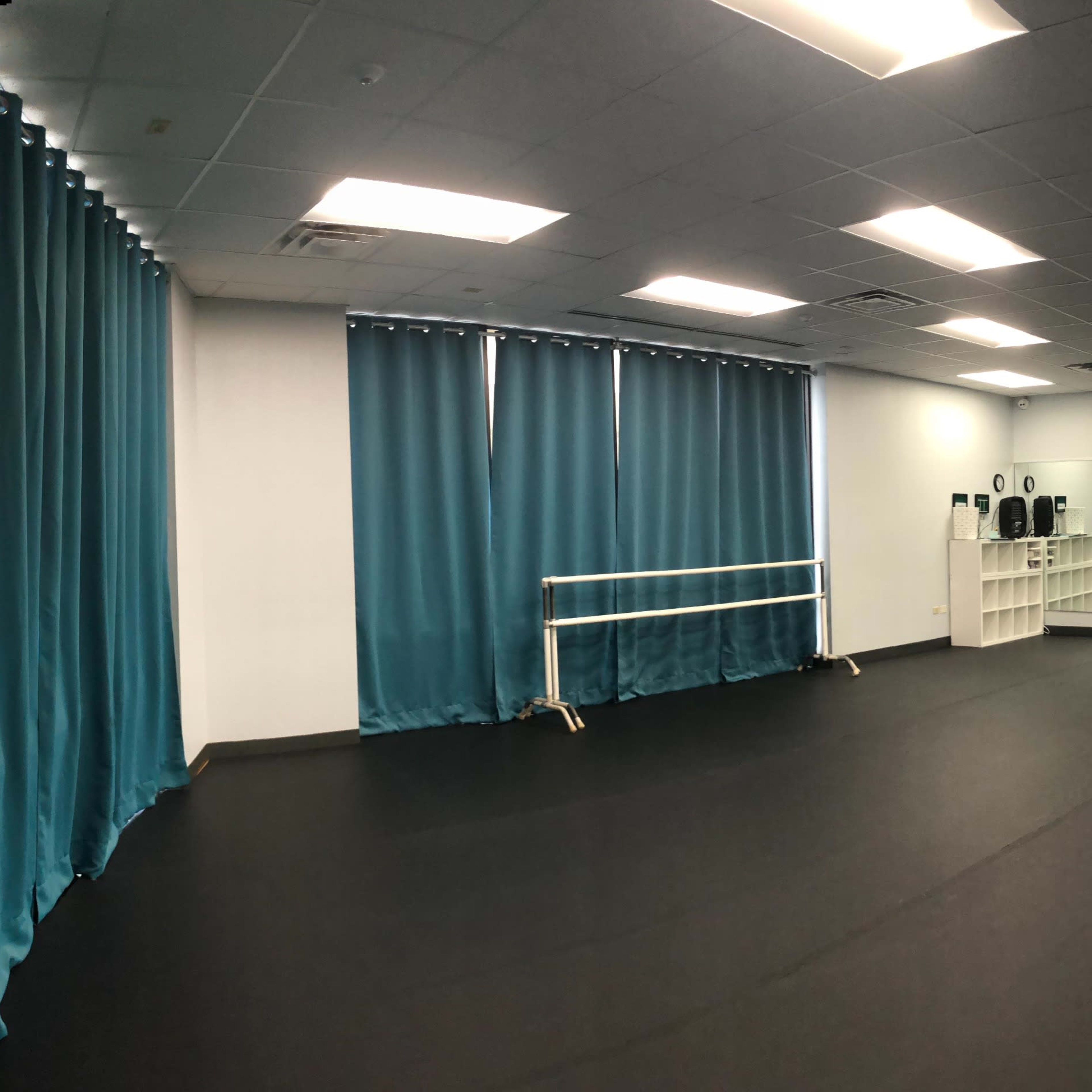 A spacious dance studio with black flooring, teal curtains, and mirrors on one wall.