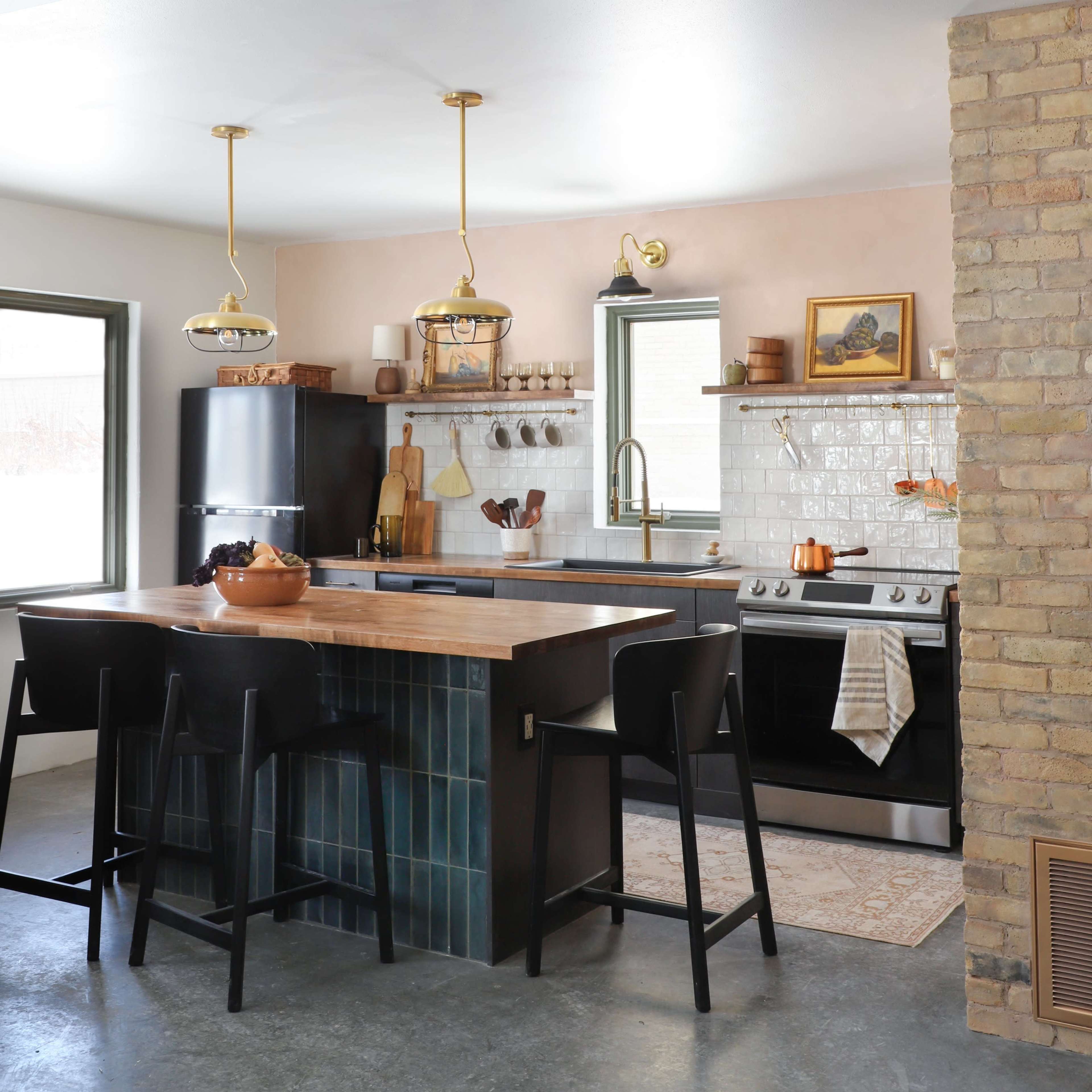 A modern kitchen with a central island featuring black stools, stainless steel appliances, and light-colored cabinetry.