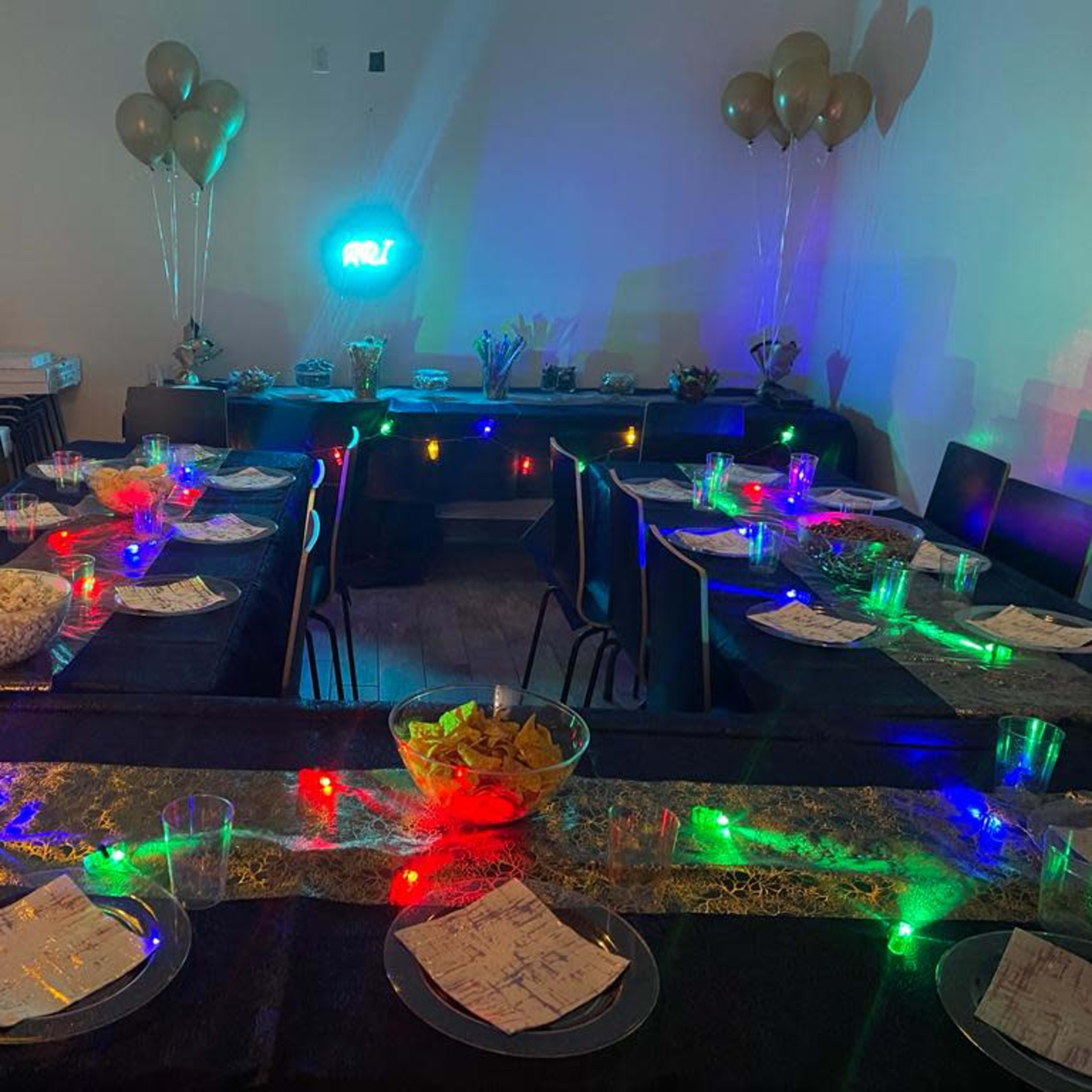 A decorated party space with tables set up, colorful lights, and snacks arranged on a buffet table.