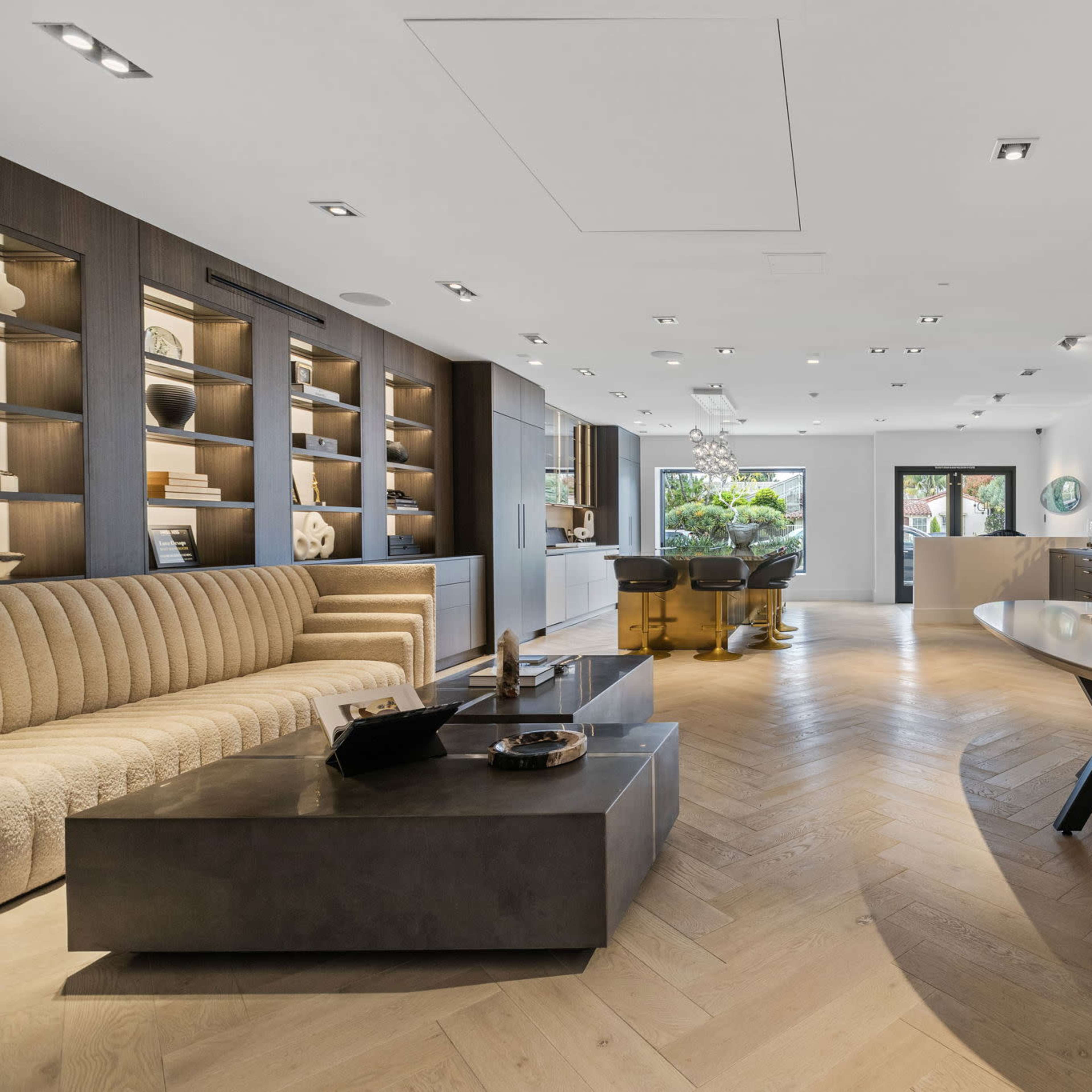A modern interior space features a stylish sofa, a large central table, and an open layout with shelves displaying decorative items.