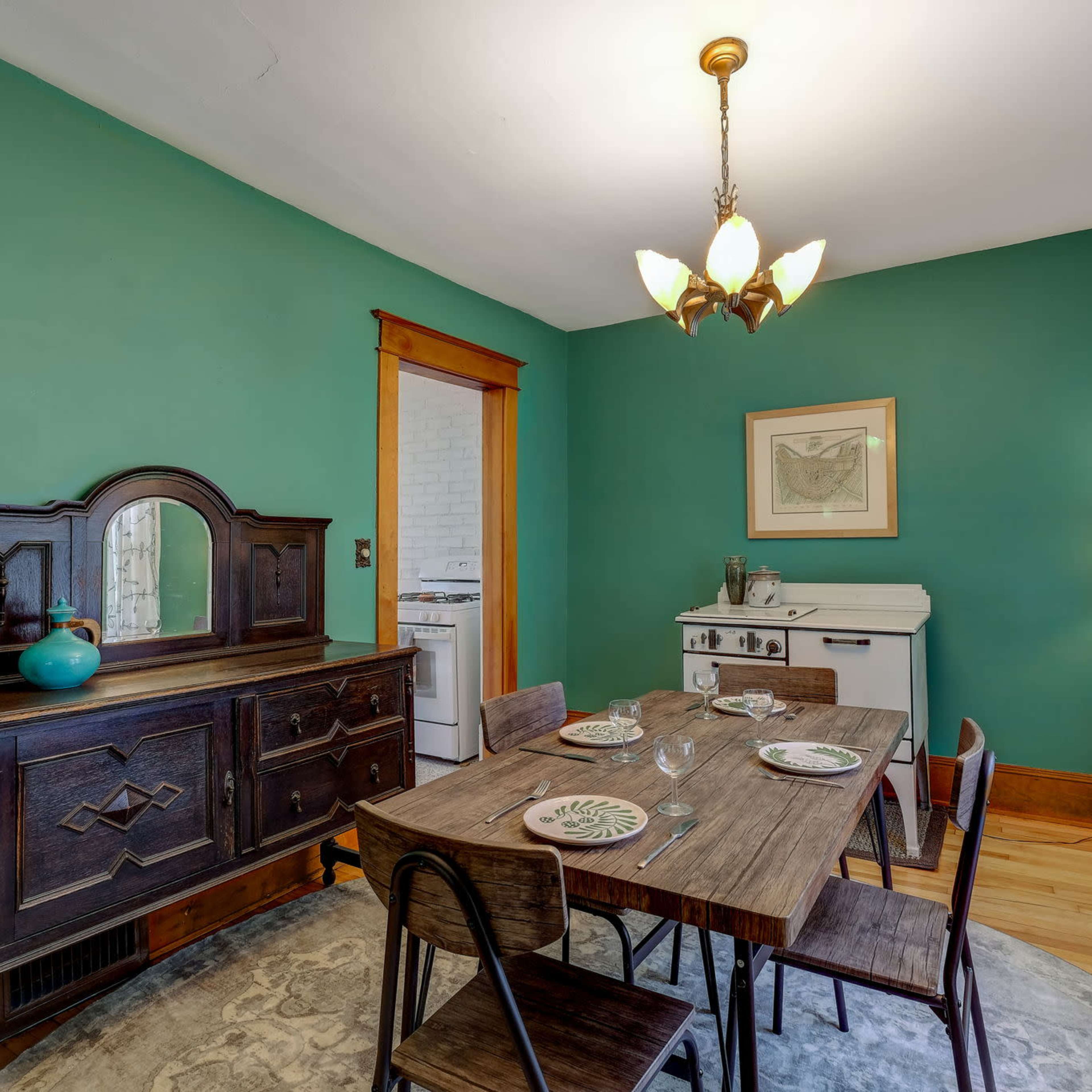 A dining room with a wooden table set with plates, a sideboard, and a vintage stove in the background against a green wall.