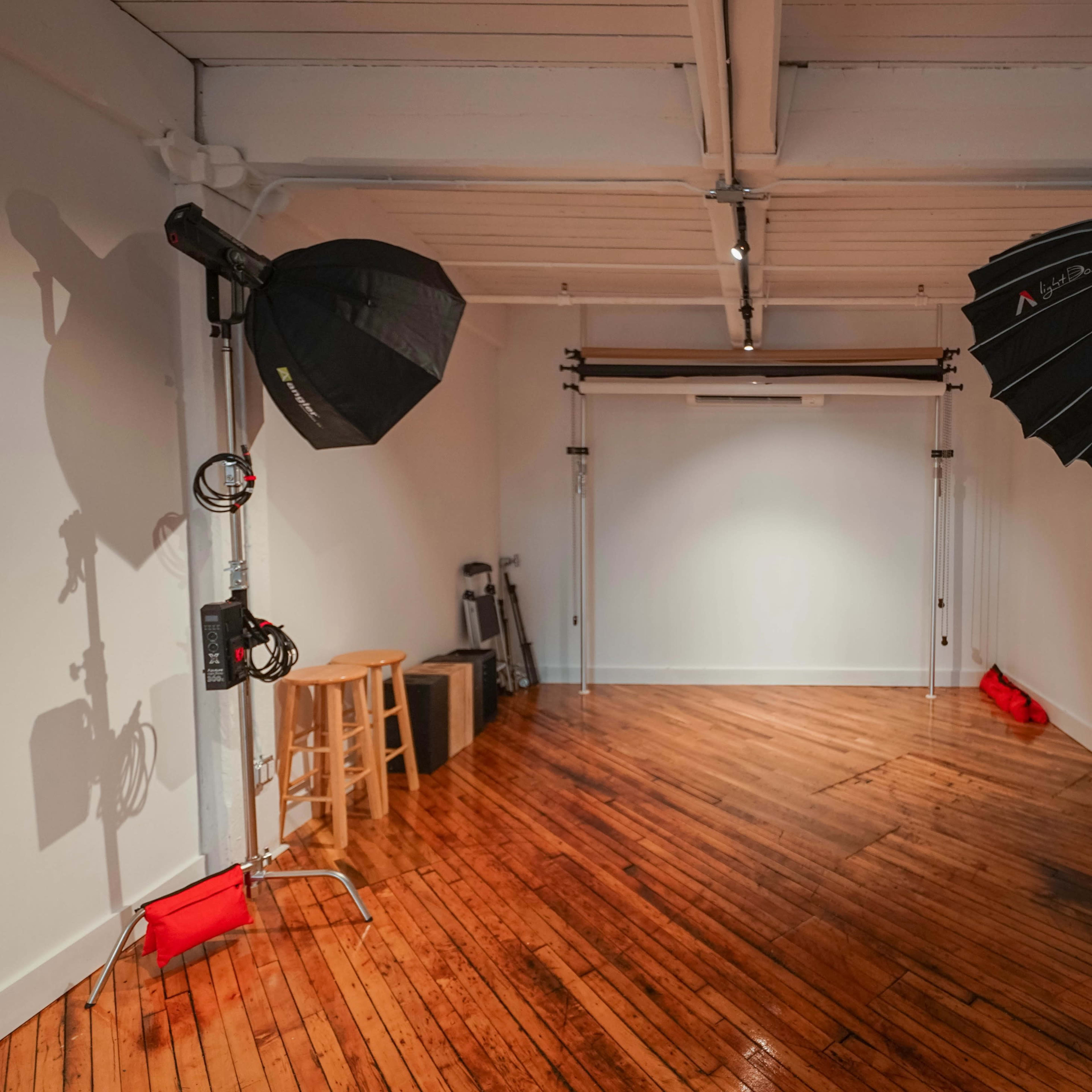 A photography studio features two large softbox lights on stands, a seamless backdrop setup, and polished wooden flooring.
