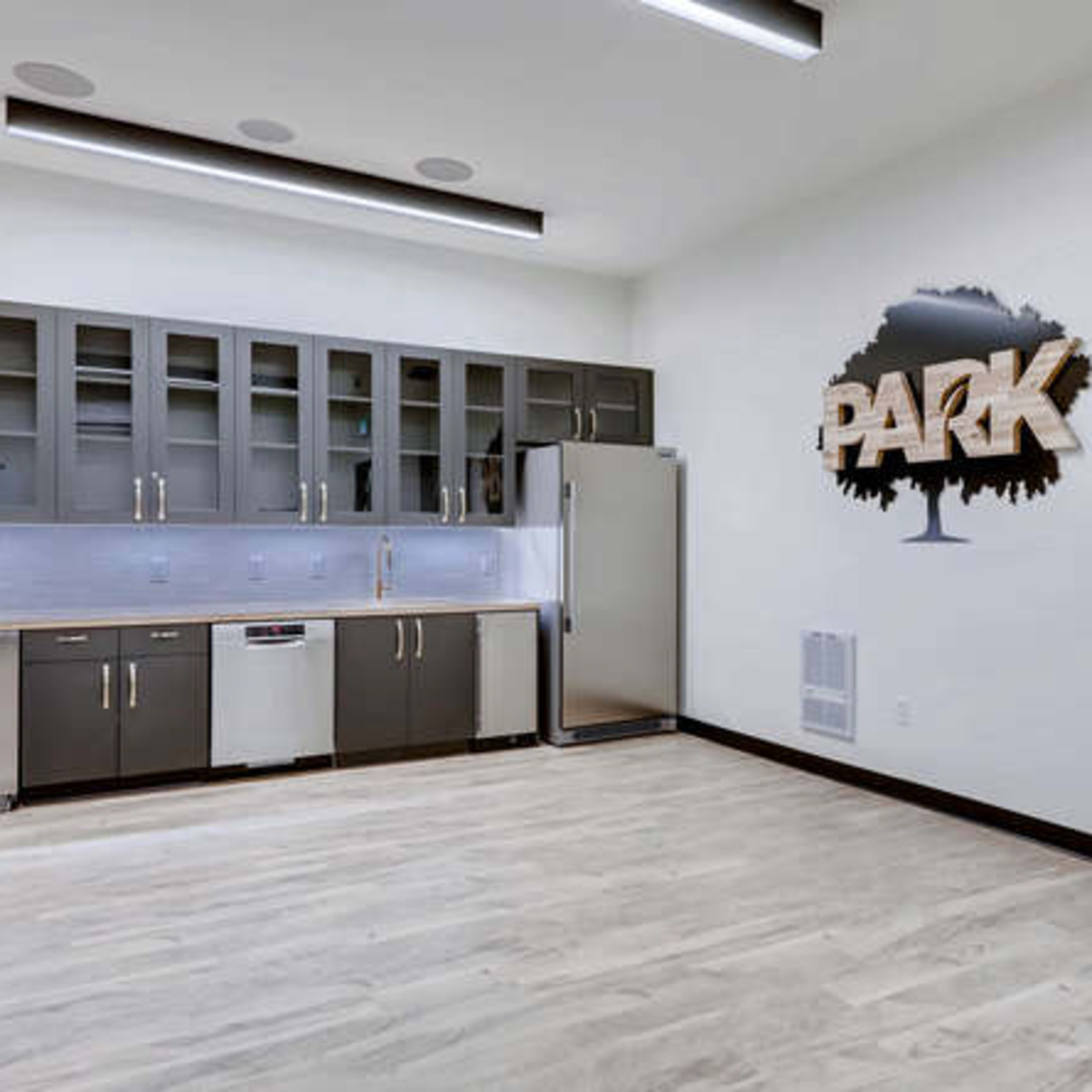 A modern kitchen area with dark cabinetry, stainless steel appliances, and a large wall display featuring the word "PARK" next to a tree graphic.