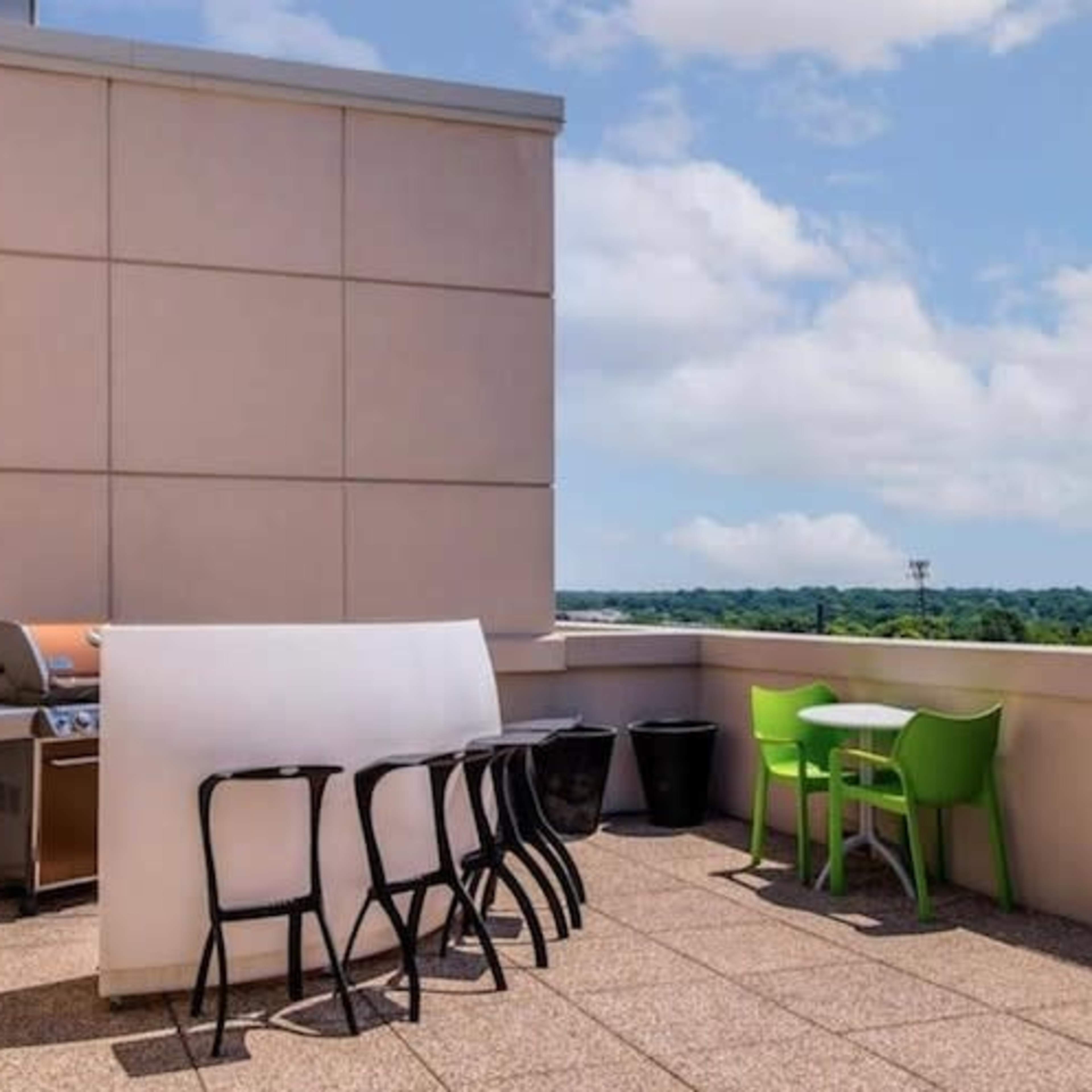 A rooftop terrace features a grill, several tables and chairs, and views of the surrounding landscape.