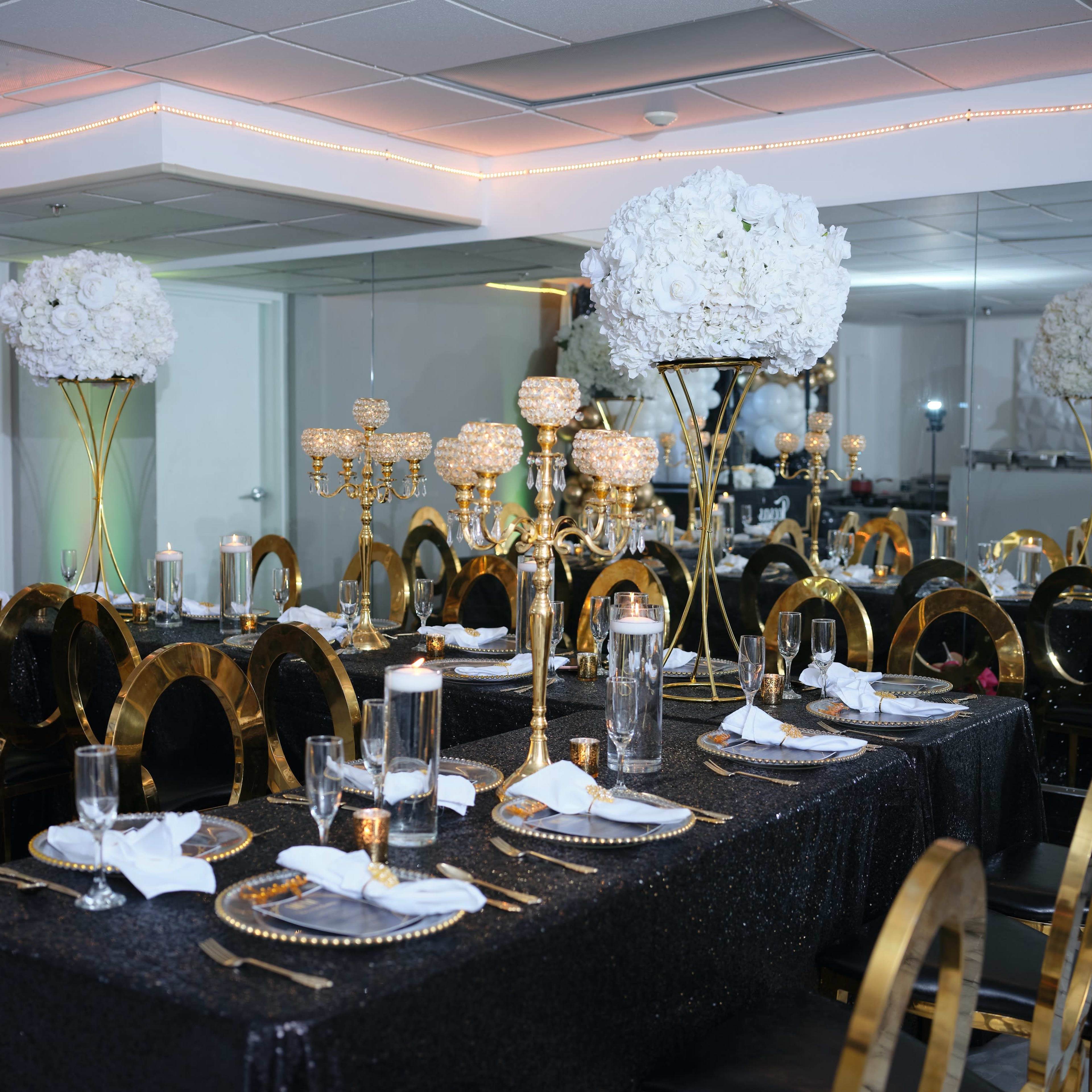 A beautifully arranged dining area with black tables draped in sequin fabric, adorned with gold accents, elegant tableware, and tall floral centerpieces.