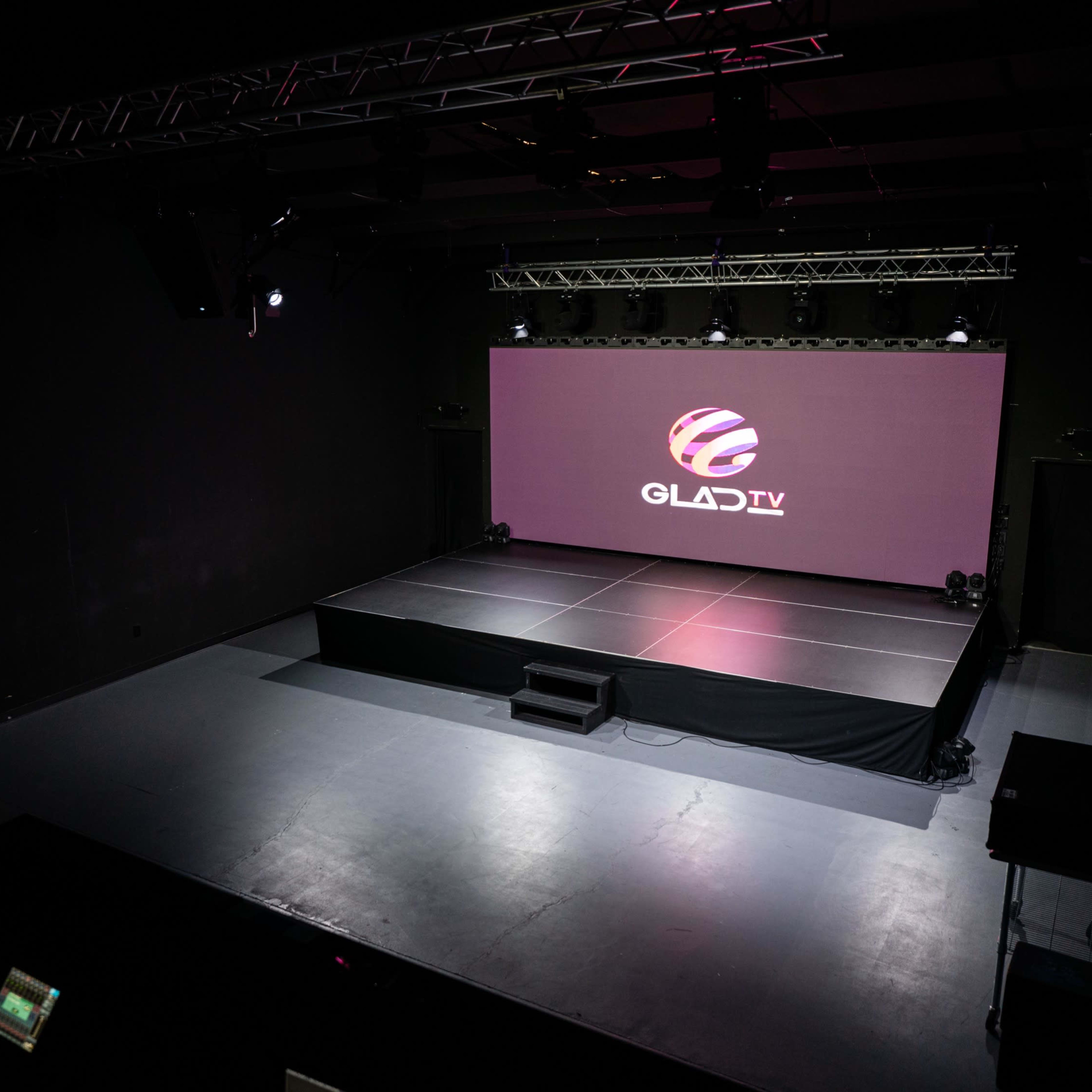A stage setup with a large screen displaying the logo for GLAD TV in a darkened room.
