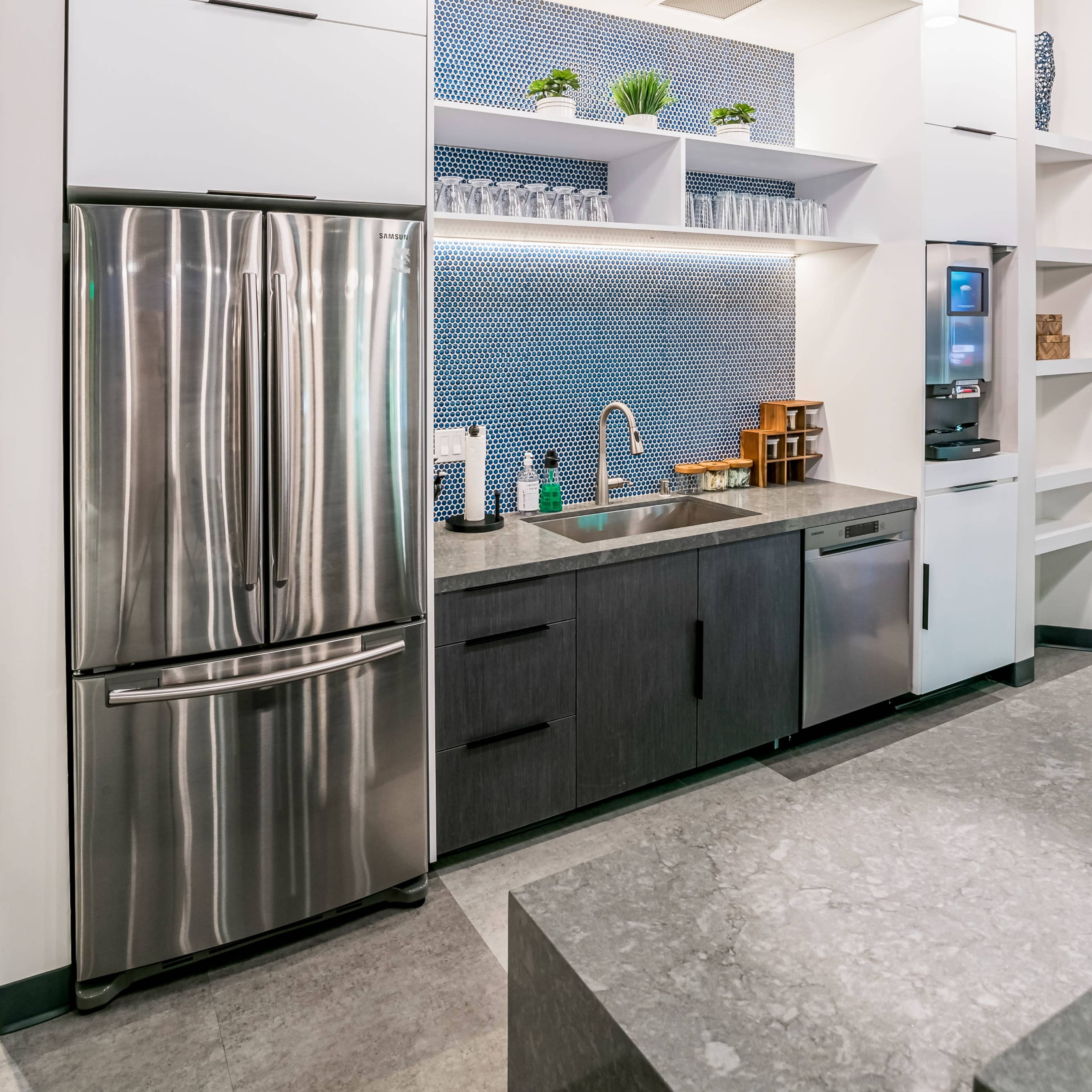 A modern kitchen featuring a stainless steel refrigerator, a sink with a faucet, and upper and lower cabinets against a blue patterned wall.