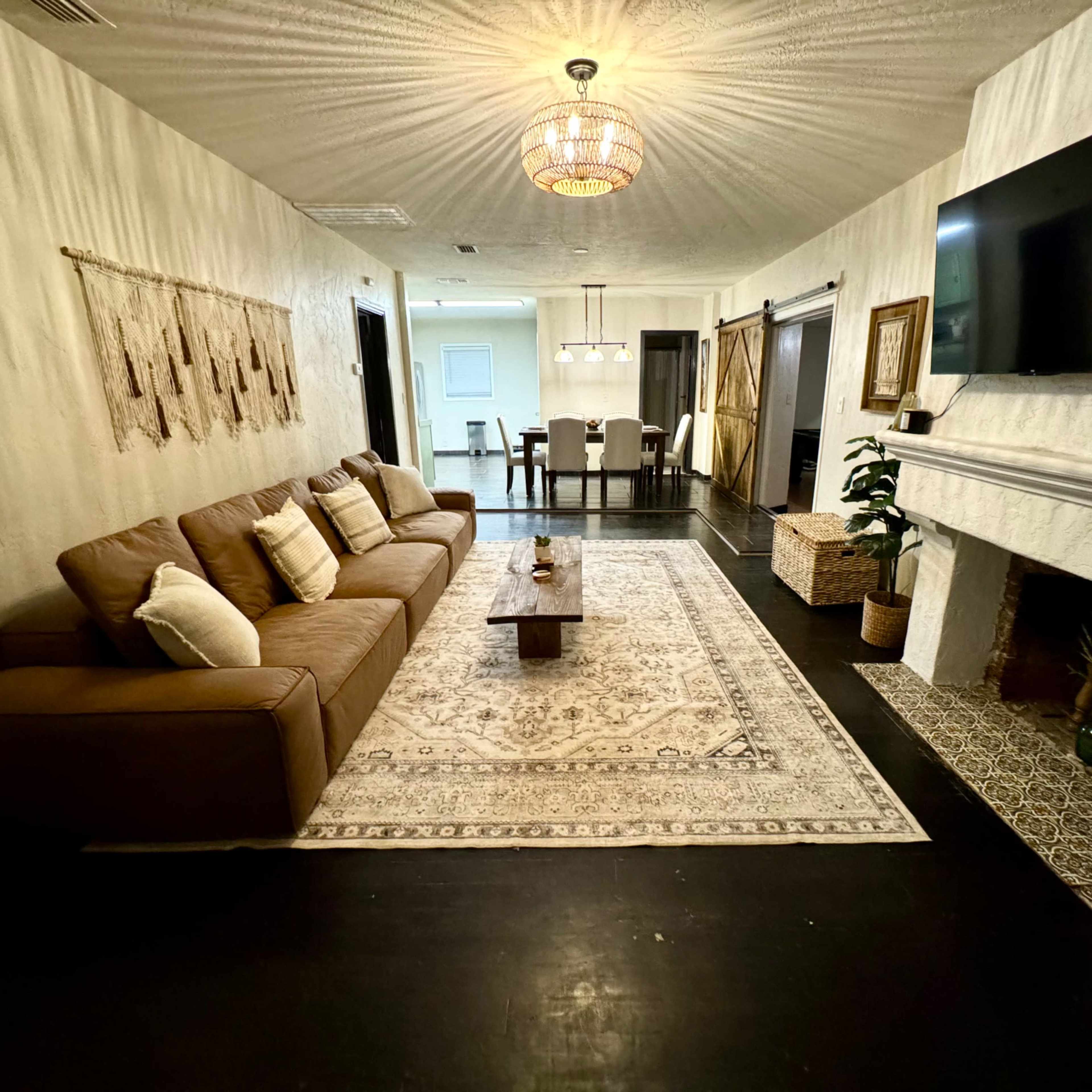 A living room with a brown sofa, a coffee table on a patterned rug, a television mounted on the wall, and a fireplace.