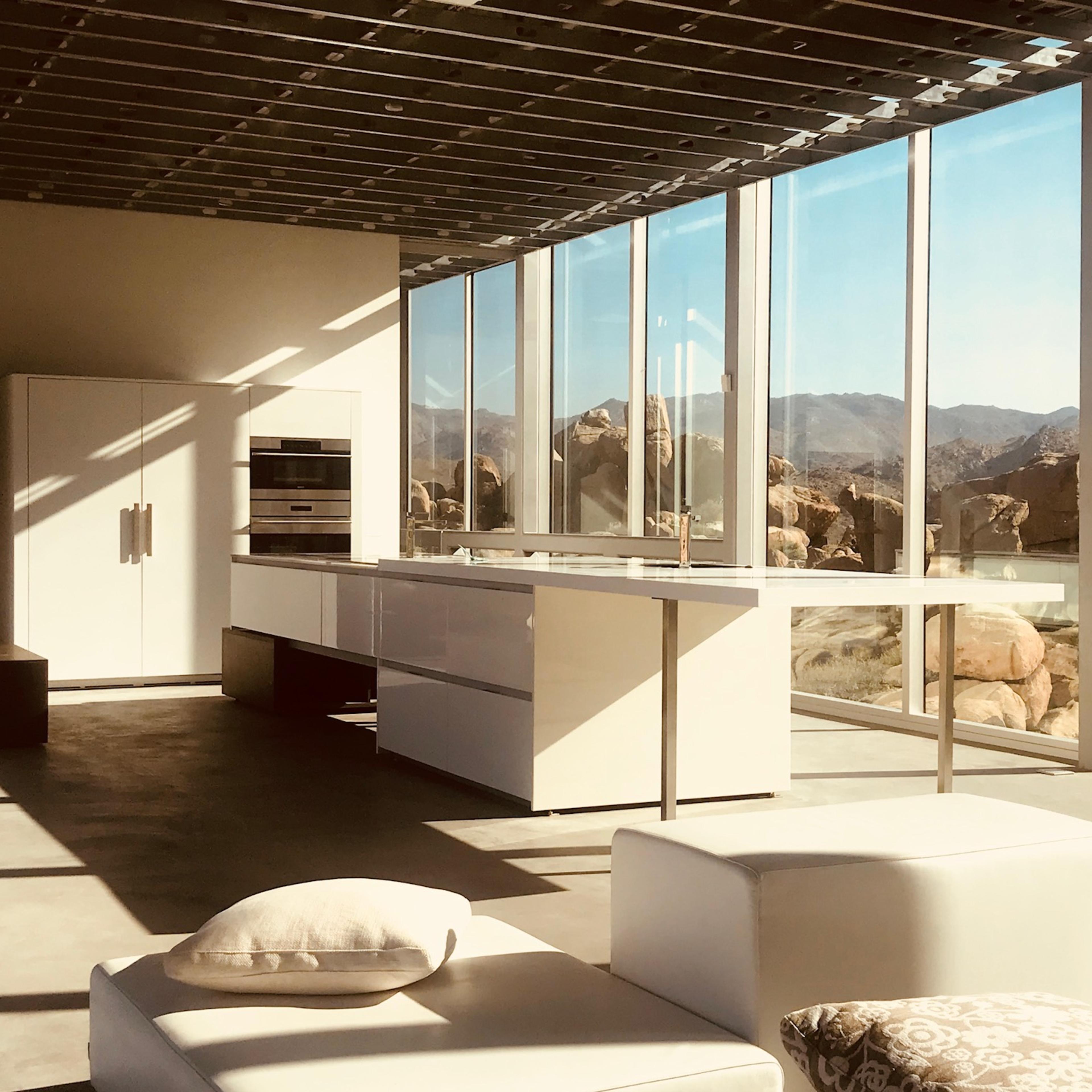 A modern kitchen with large windows overlooking rocky mountains and a clear blue sky.