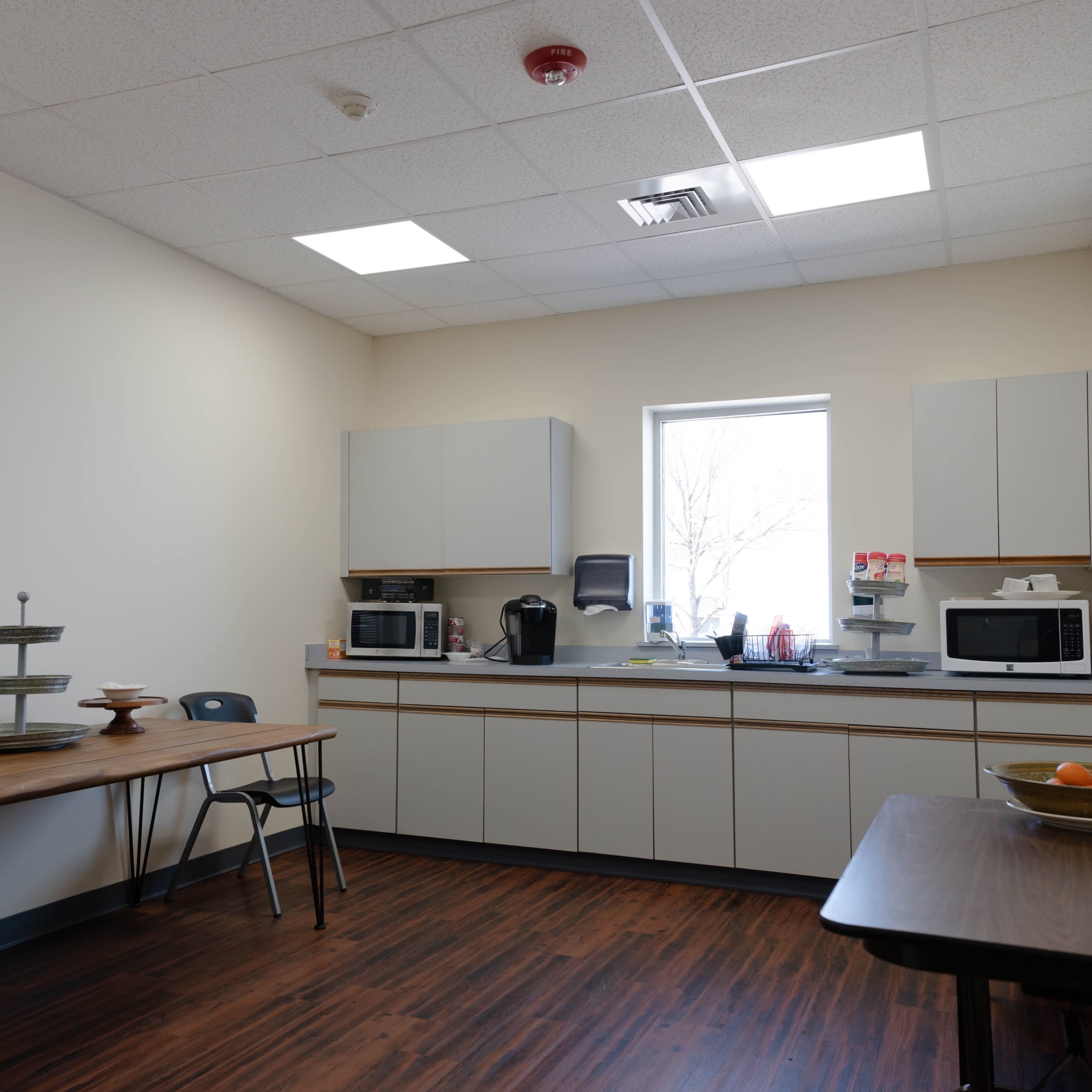 A break room with a table, chairs, and a kitchenette featuring microwaves and a window.