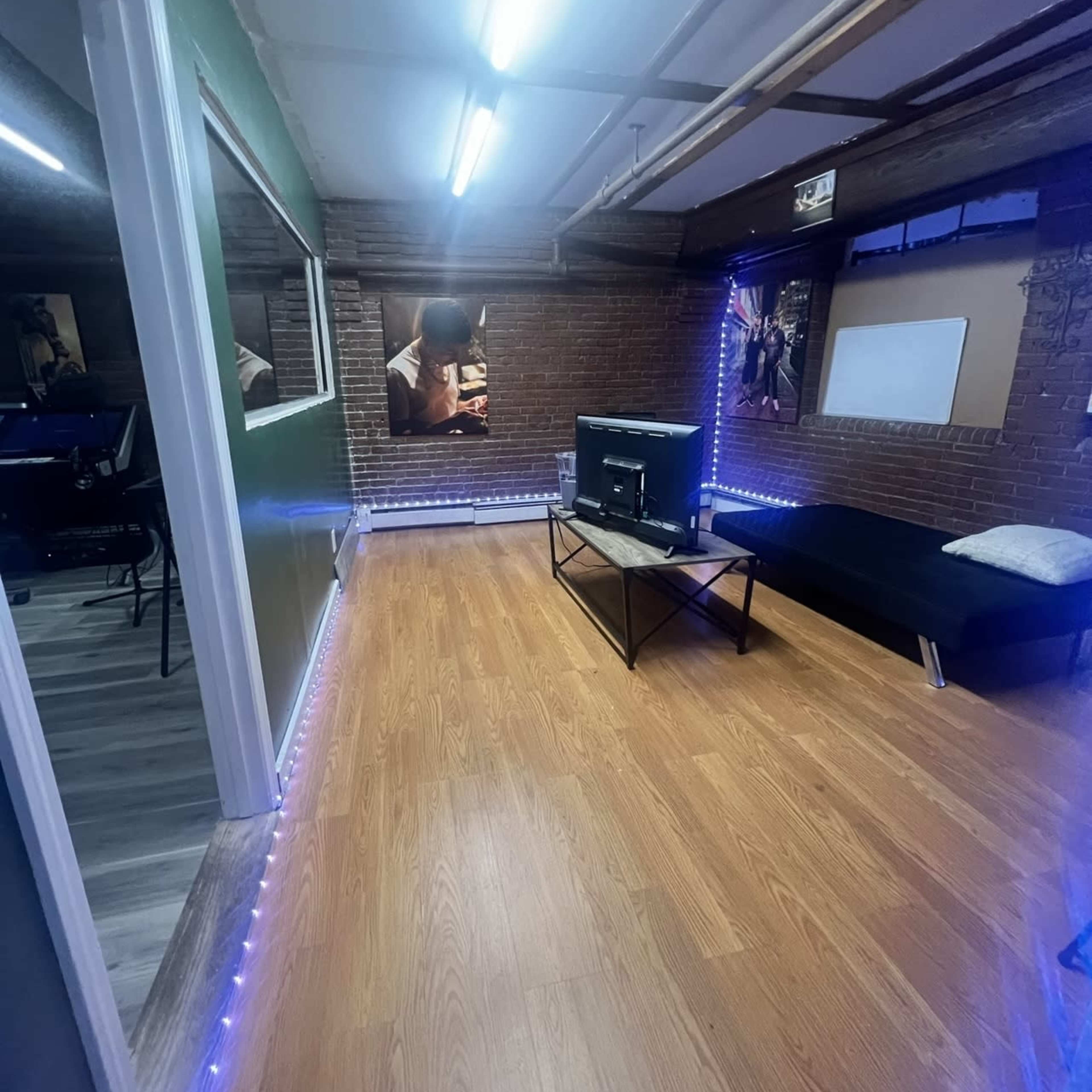 A room with wooden flooring, a black sofa, a coffee table, and LED strip lighting along the walls.