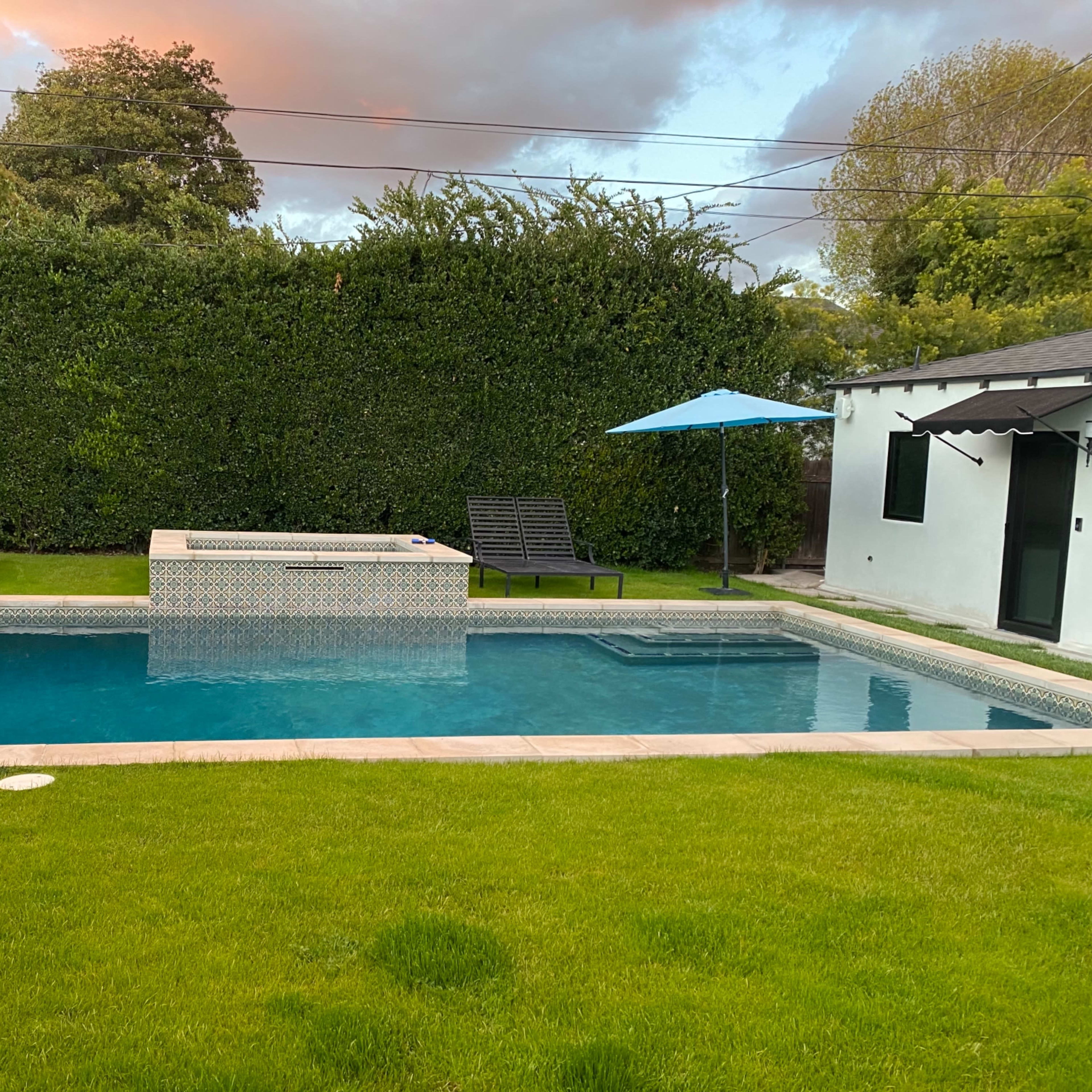 A swimming pool surrounded by green grass, two lounge chairs, and an umbrella in a backyard setting.