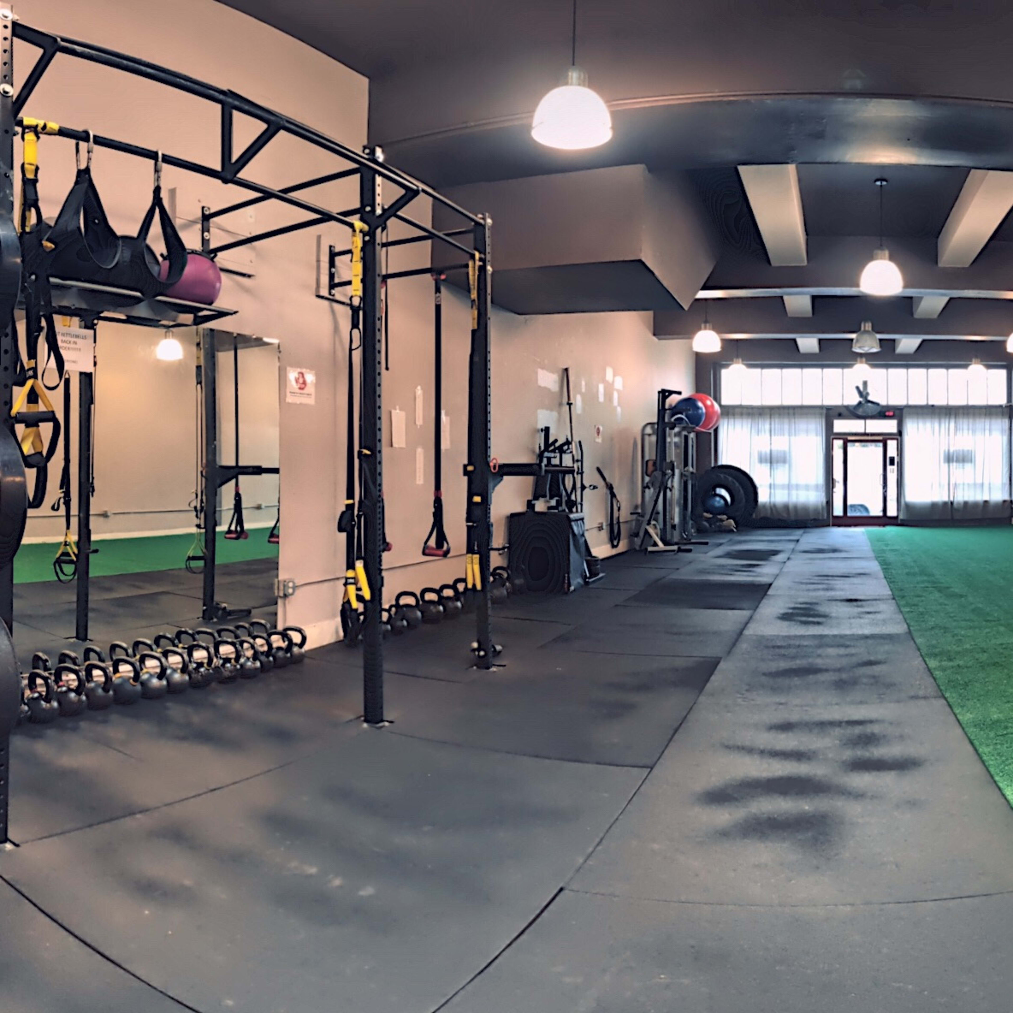 A spacious gym with rubber flooring, exercise equipment on one side, and a large window allowing natural light to enter.