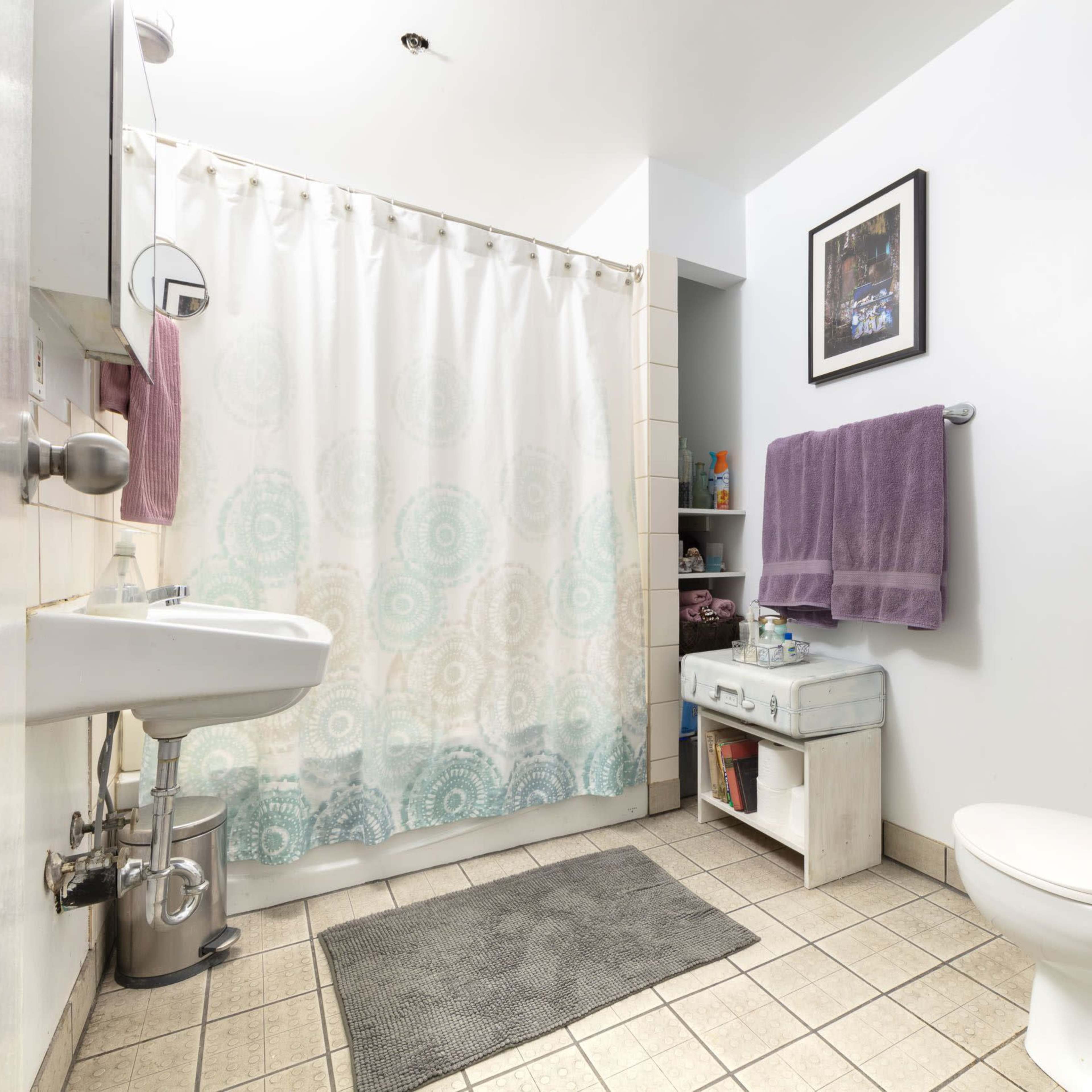 A bathroom featuring a shower curtain, a sink, a toilet, and shelves with various items.