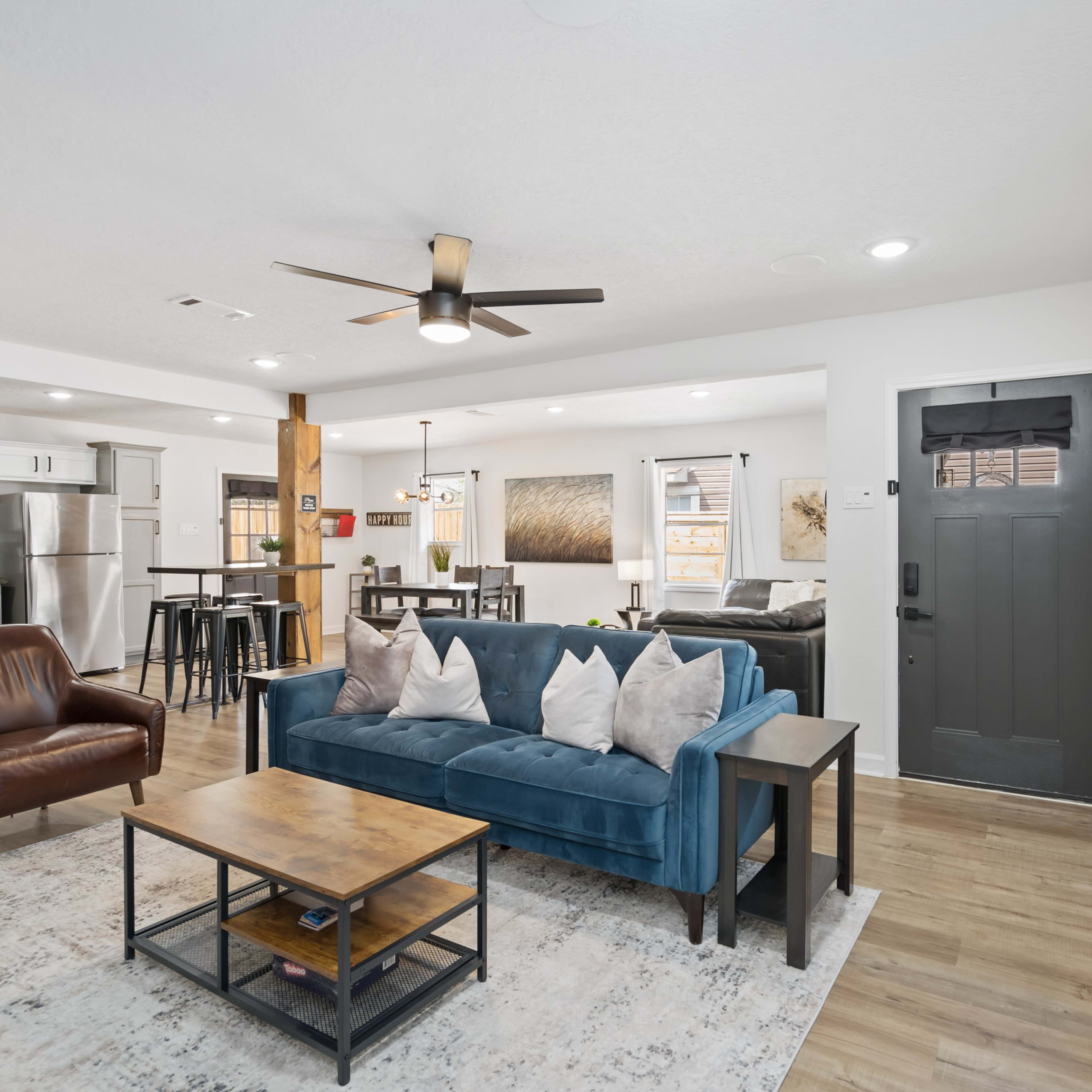 A well-furnished living area featuring a blue sofa, a wooden coffee table, and a dining space with a kitchen visible in the background.