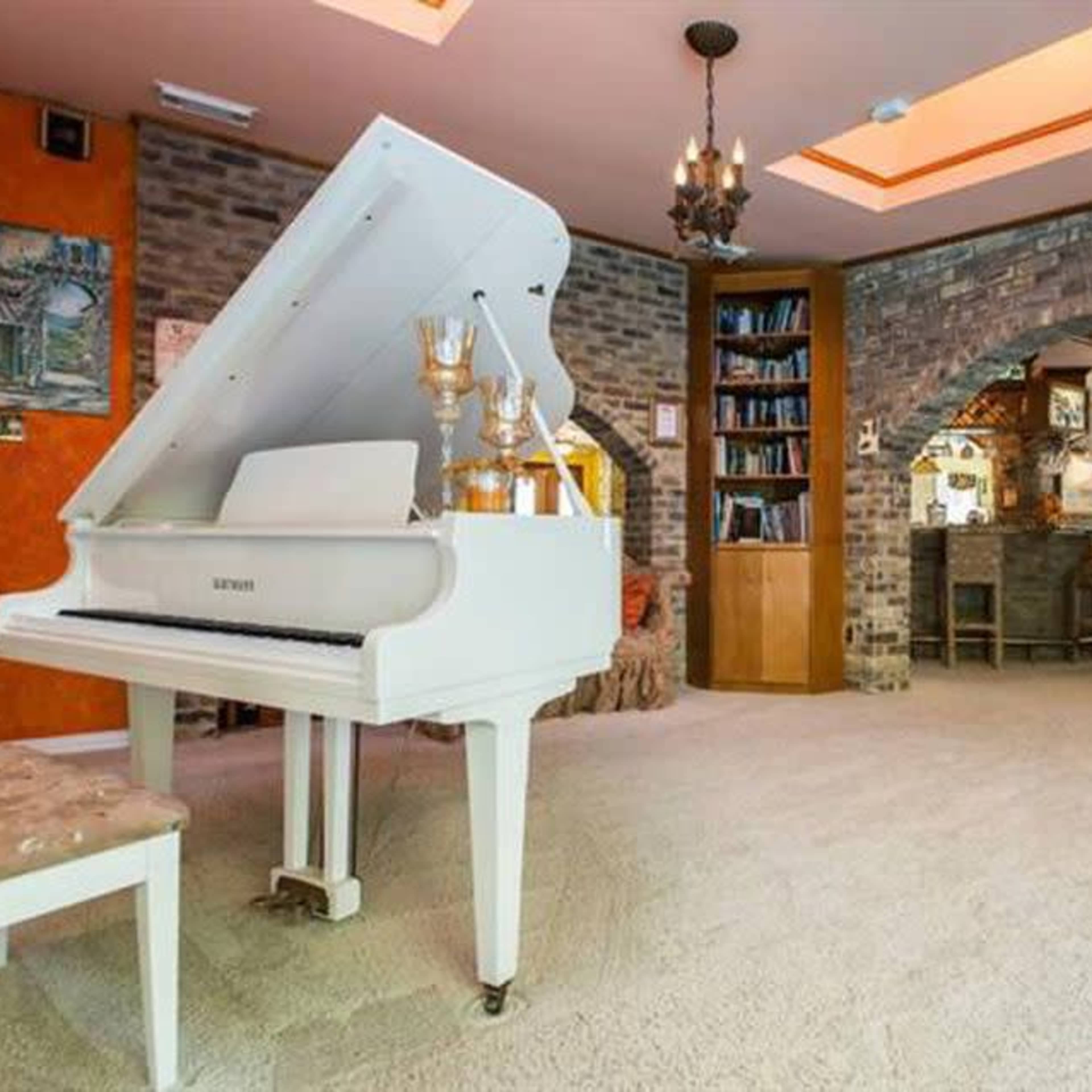 An elegantly decorated room featuring a white grand piano, brick walls, a bookshelf, and an archway leading to another area.