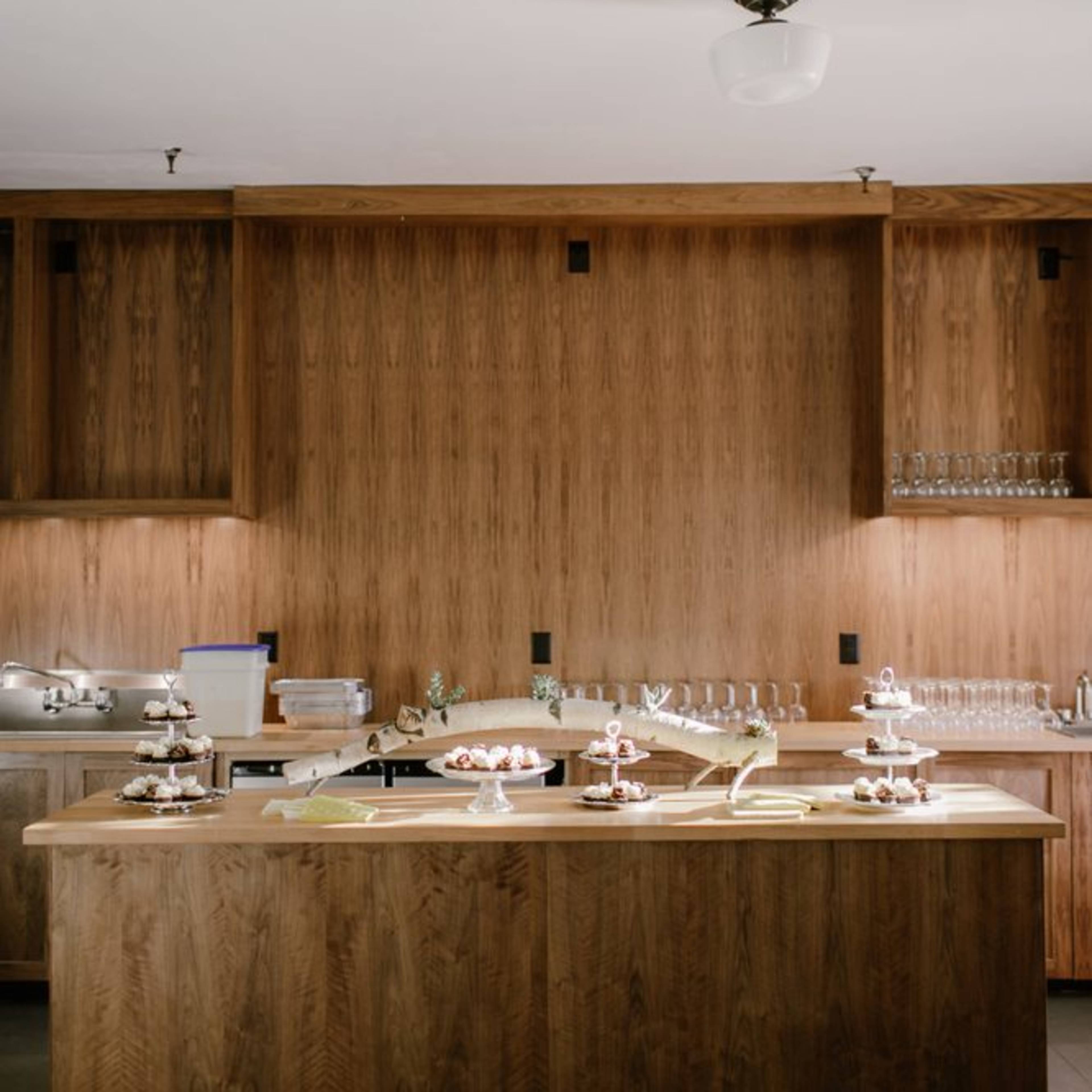 A wooden kitchen island with various desserts and a backdrop of wooden cabinetry and glassware.