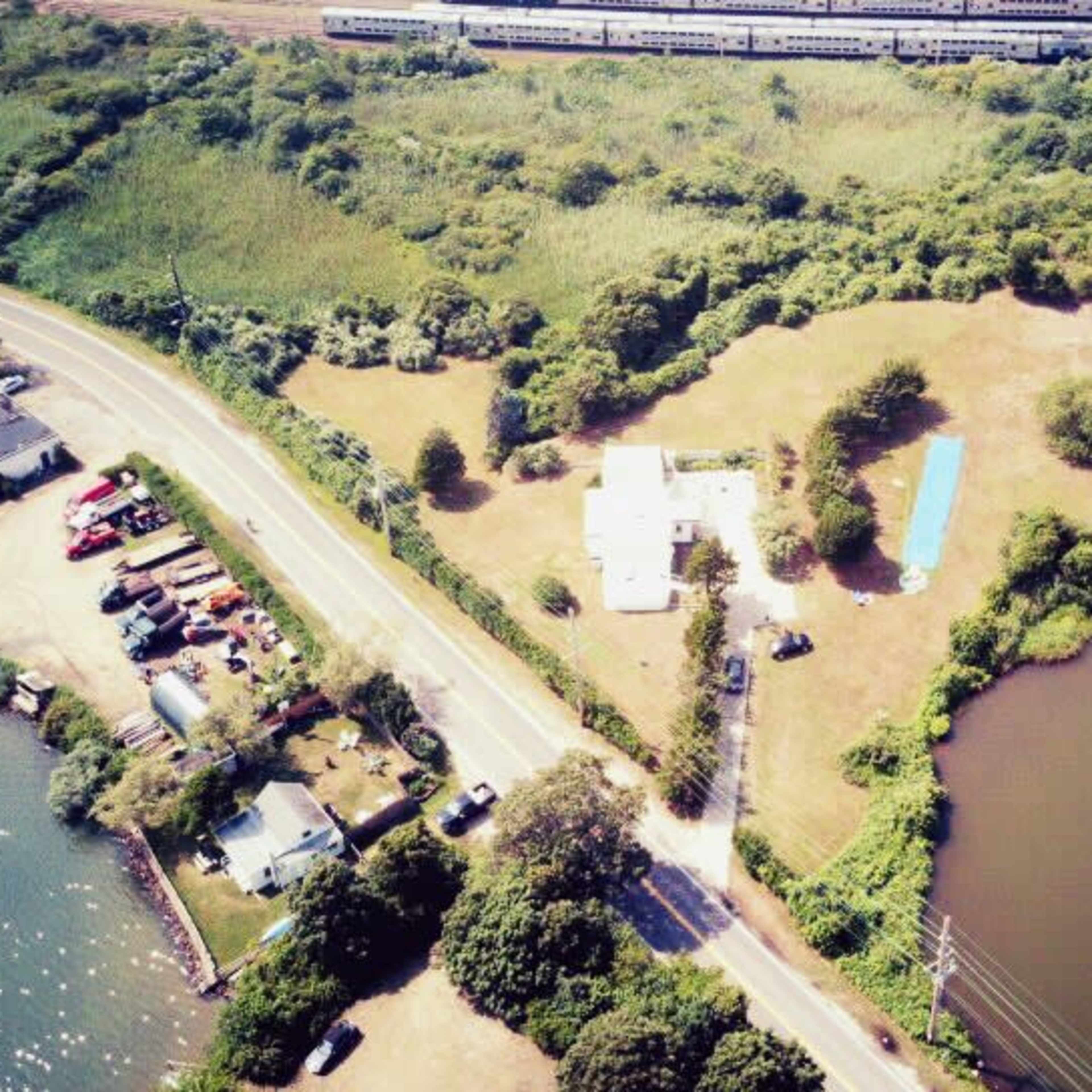 An aerial view of a property near a river, with a house, a pool, and dense greenery surrounding the area.