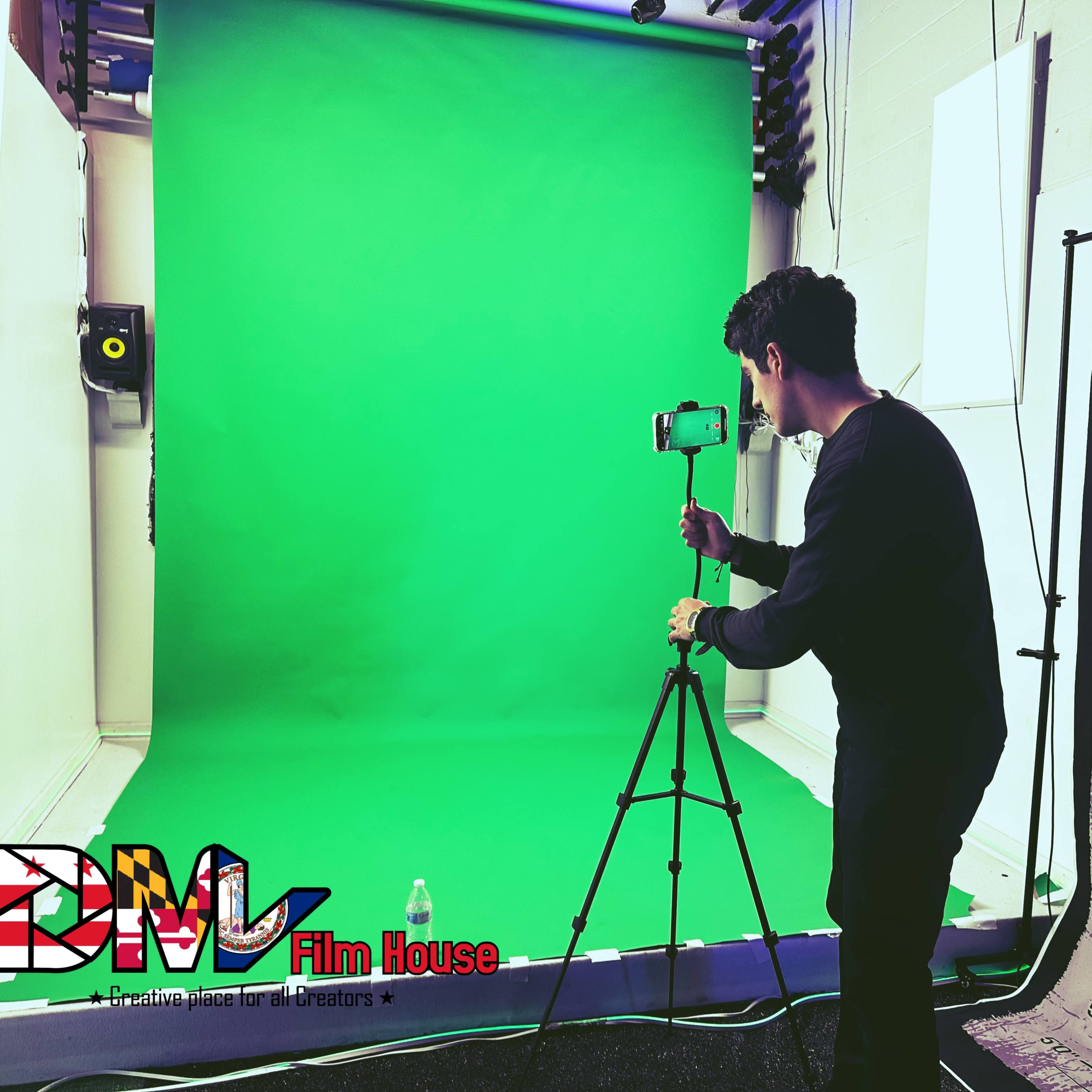 A person sets up a smartphone on a tripod in front of a green screen in a film studio.