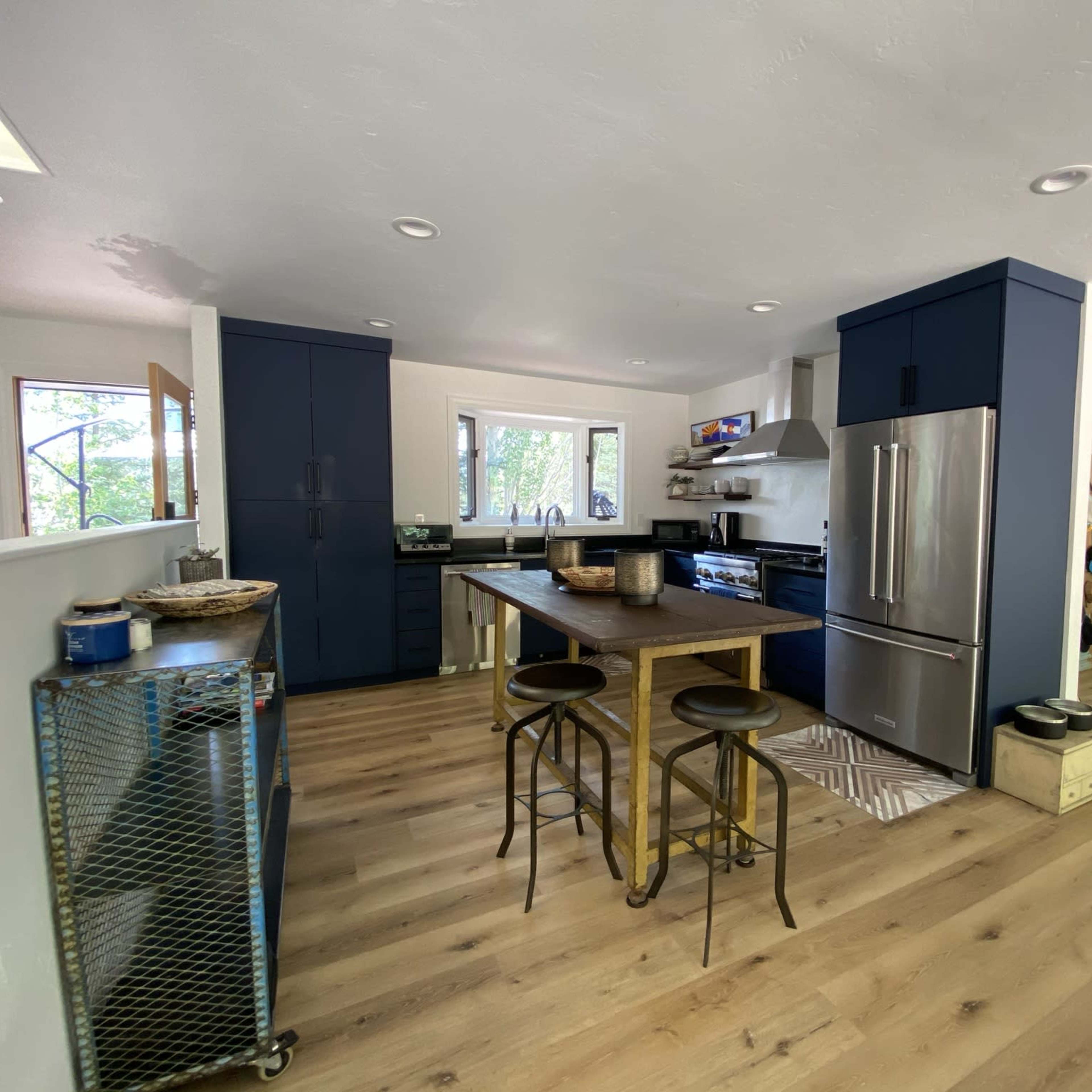 A modern kitchen with dark blue cabinets, stainless steel appliances, and a wooden dining table with metal chairs.
