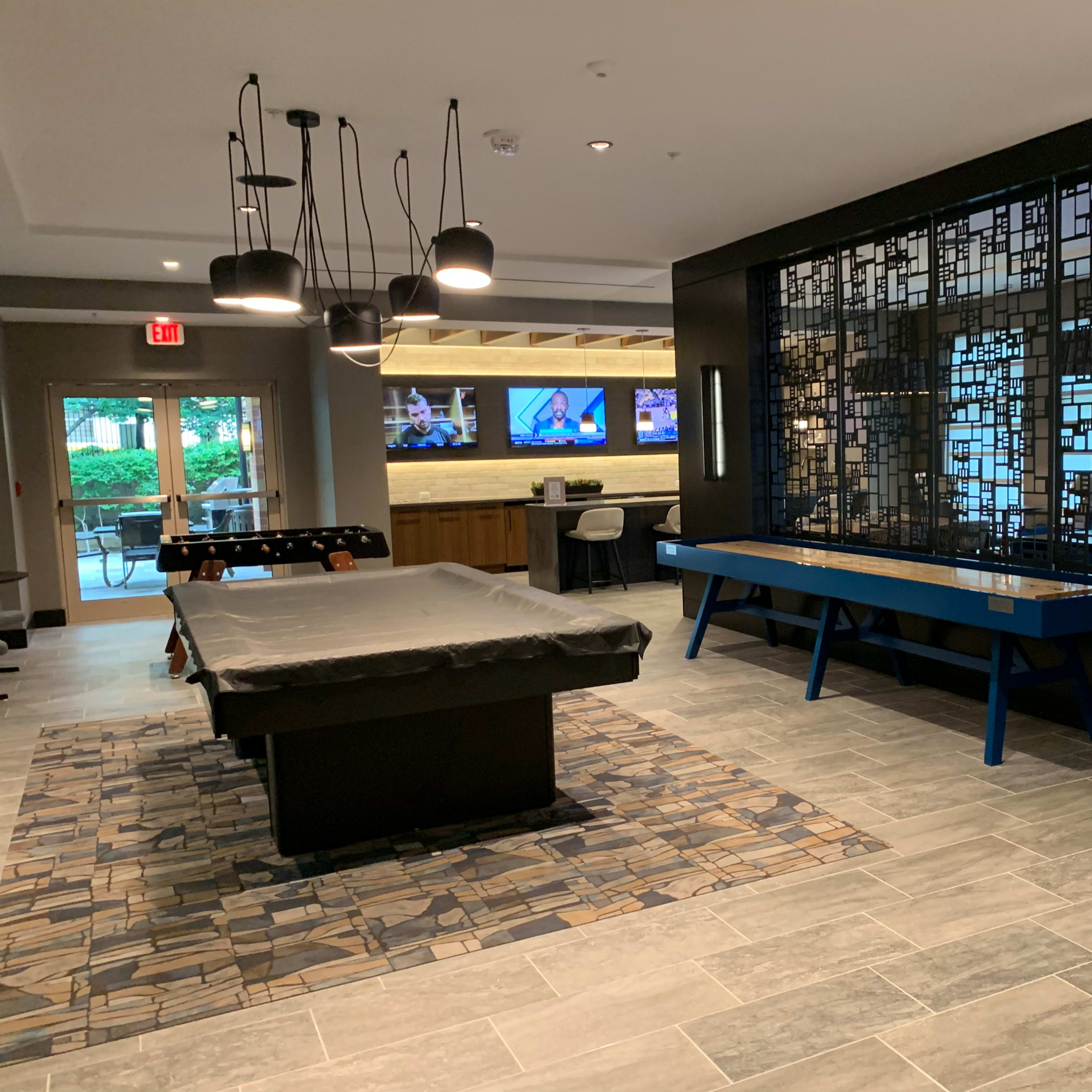 A modern recreation room featuring a pool table, a decorative wall panel, and screens mounted on the wall displaying sports.