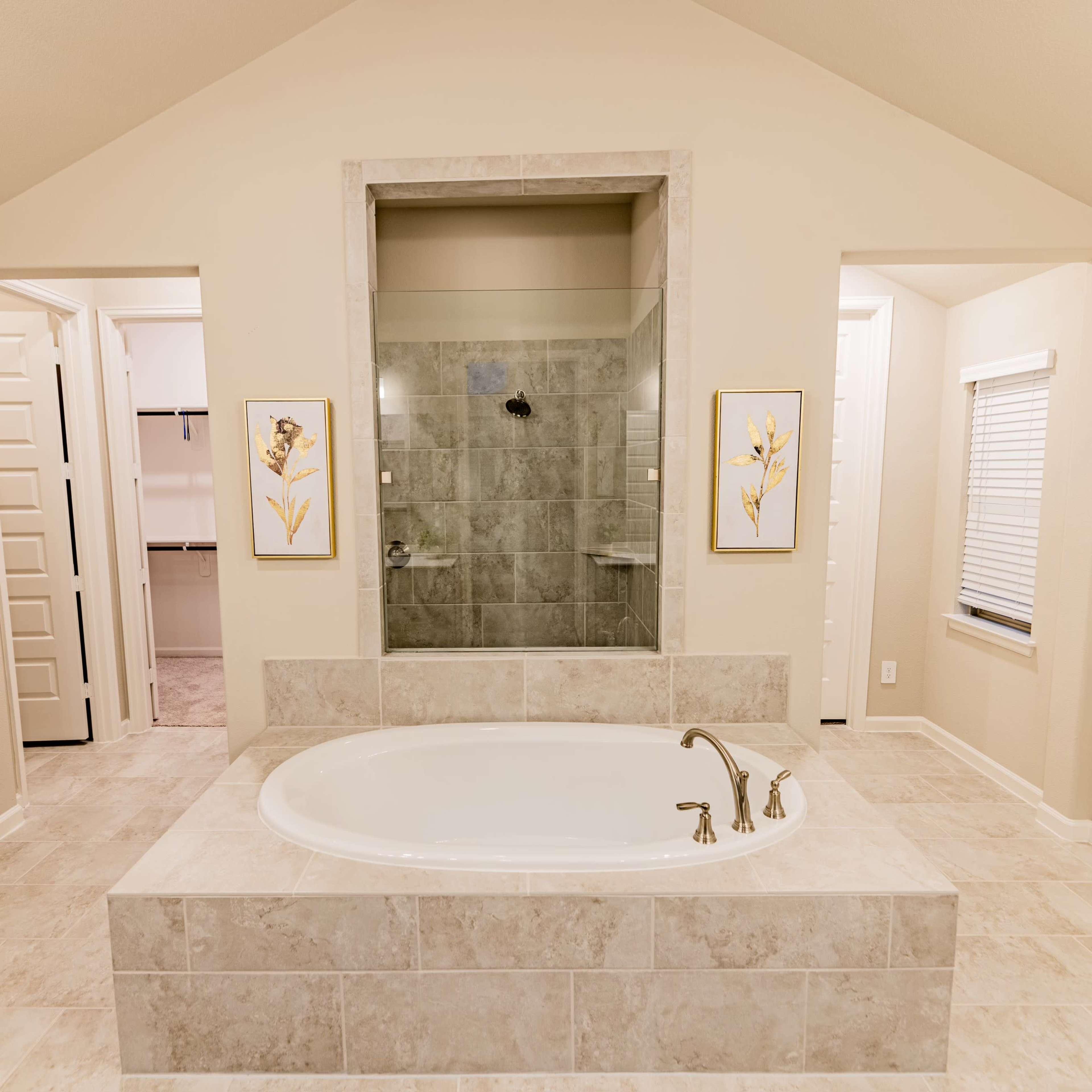A spacious bathroom featuring a freestanding bathtub, a glass shower, and two doorways leading to separate areas.