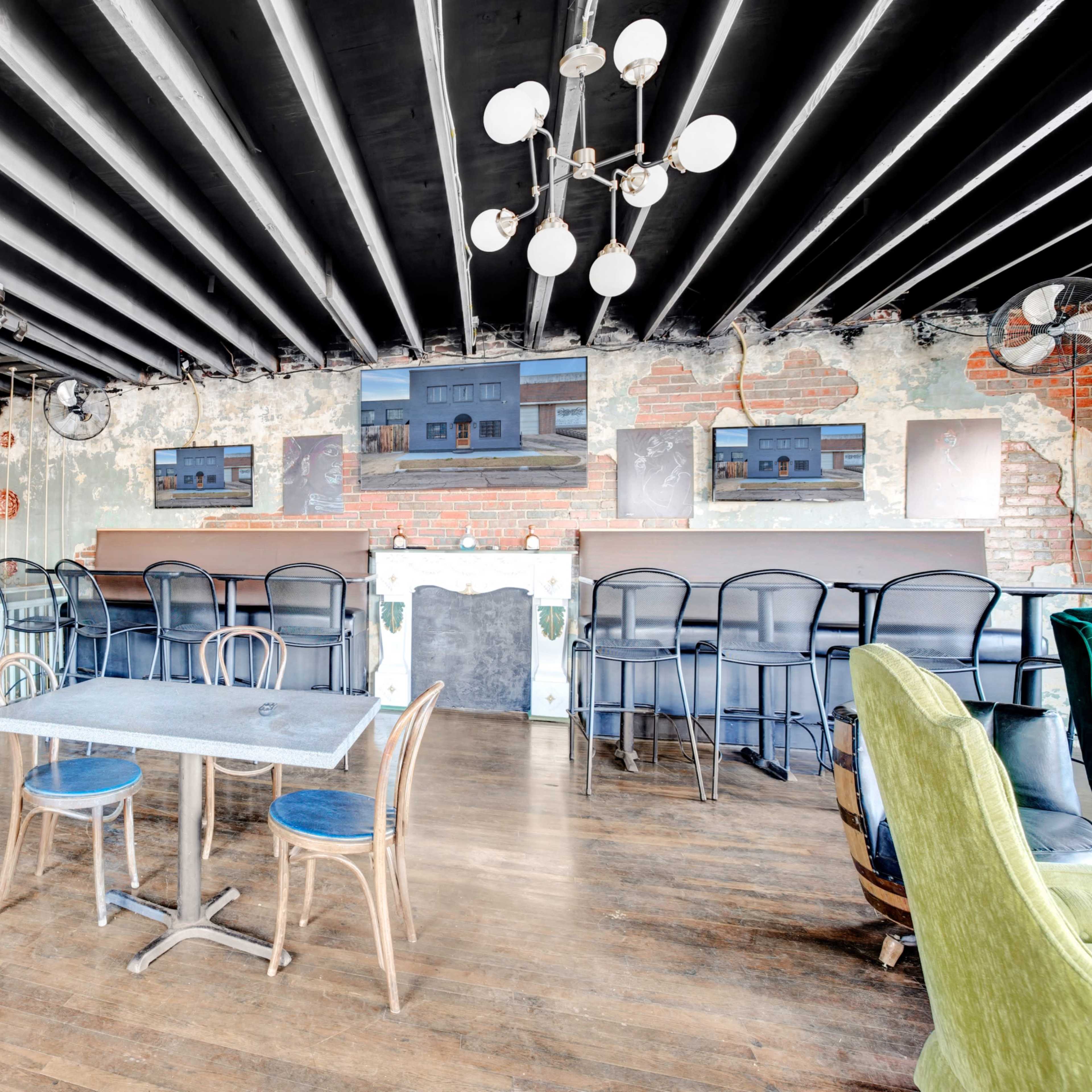 An interior space with a mix of exposed brick walls and wooden flooring, featuring a table and chairs, along with a bar area in the background.