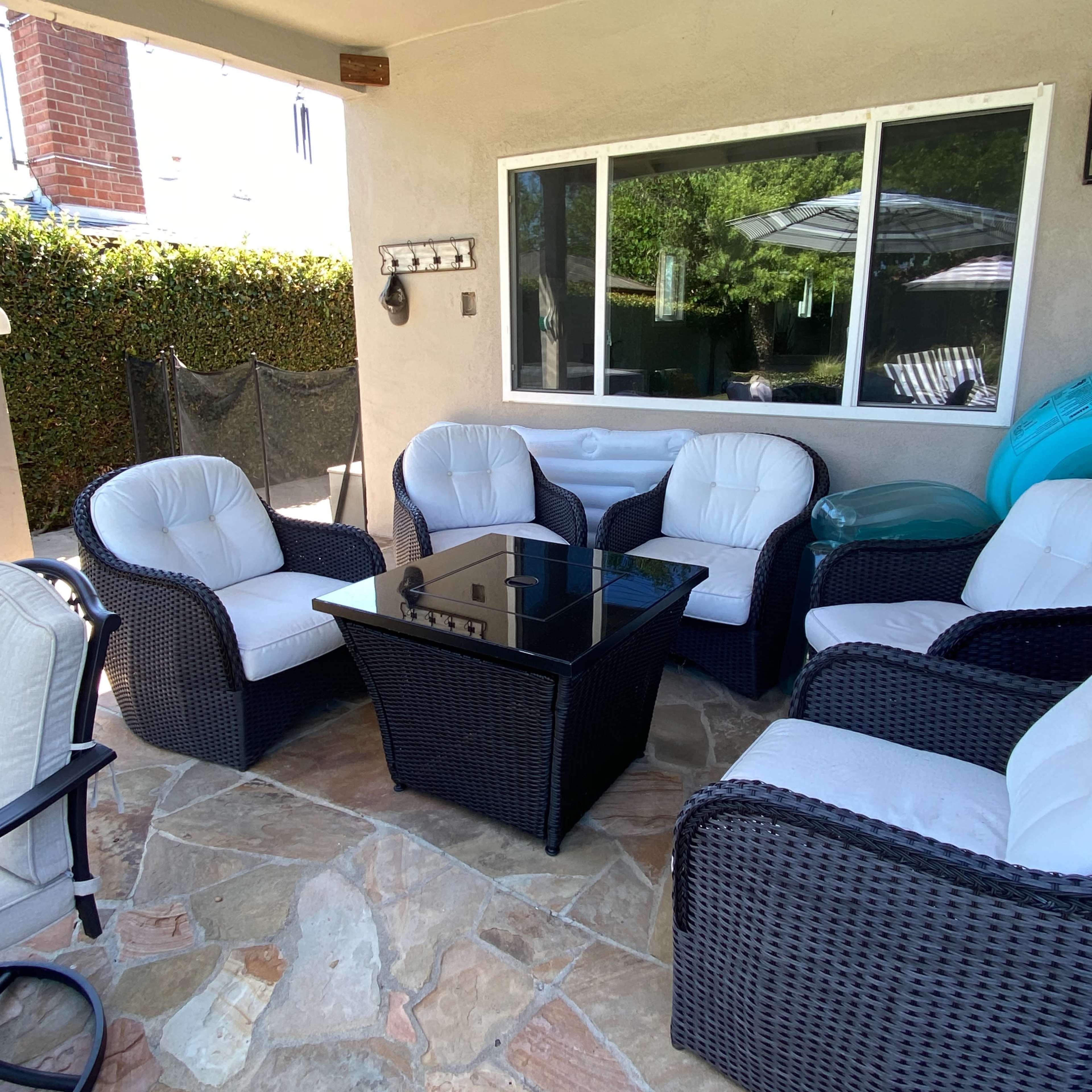 A covered patio space features four cushioned chairs arranged around a glass-top table on a stone floor.