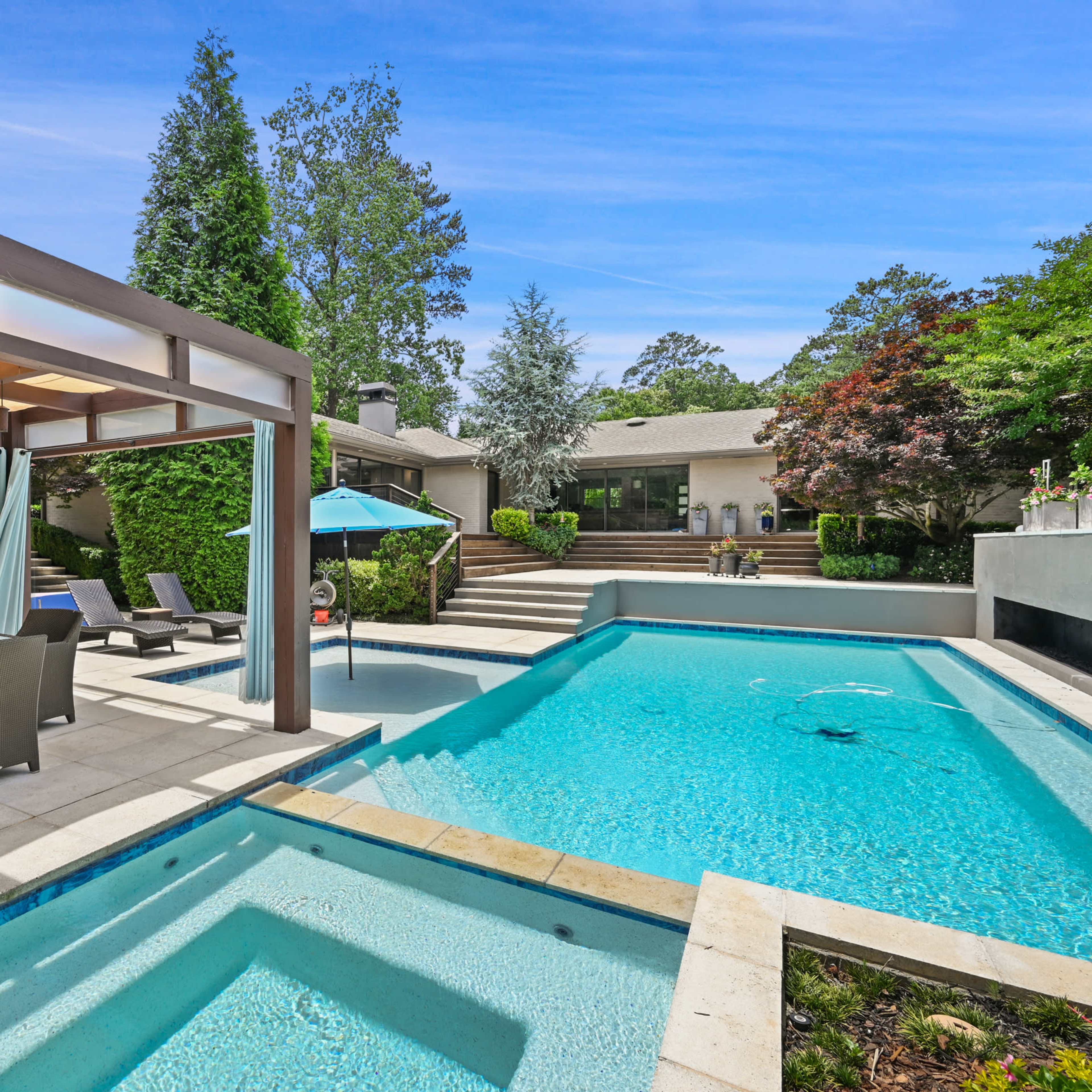A well-maintained backyard featuring a swimming pool, a covered seating area, and a landscaped garden with trees.