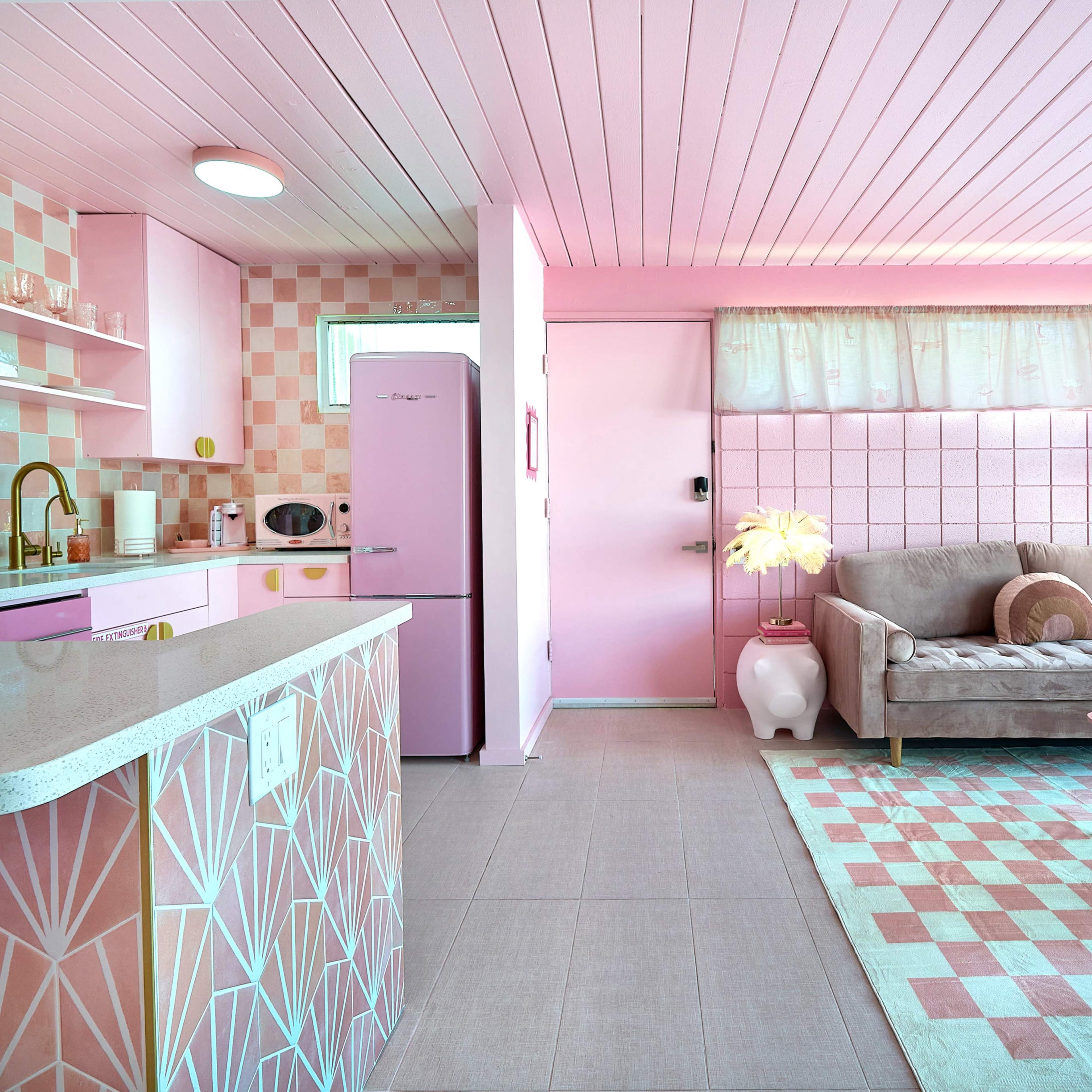 The scene features a brightly colored kitchen and living area, predominantly in shades of pink, with a modern design that includes a sofa, a coffee table, and coordinated decor.