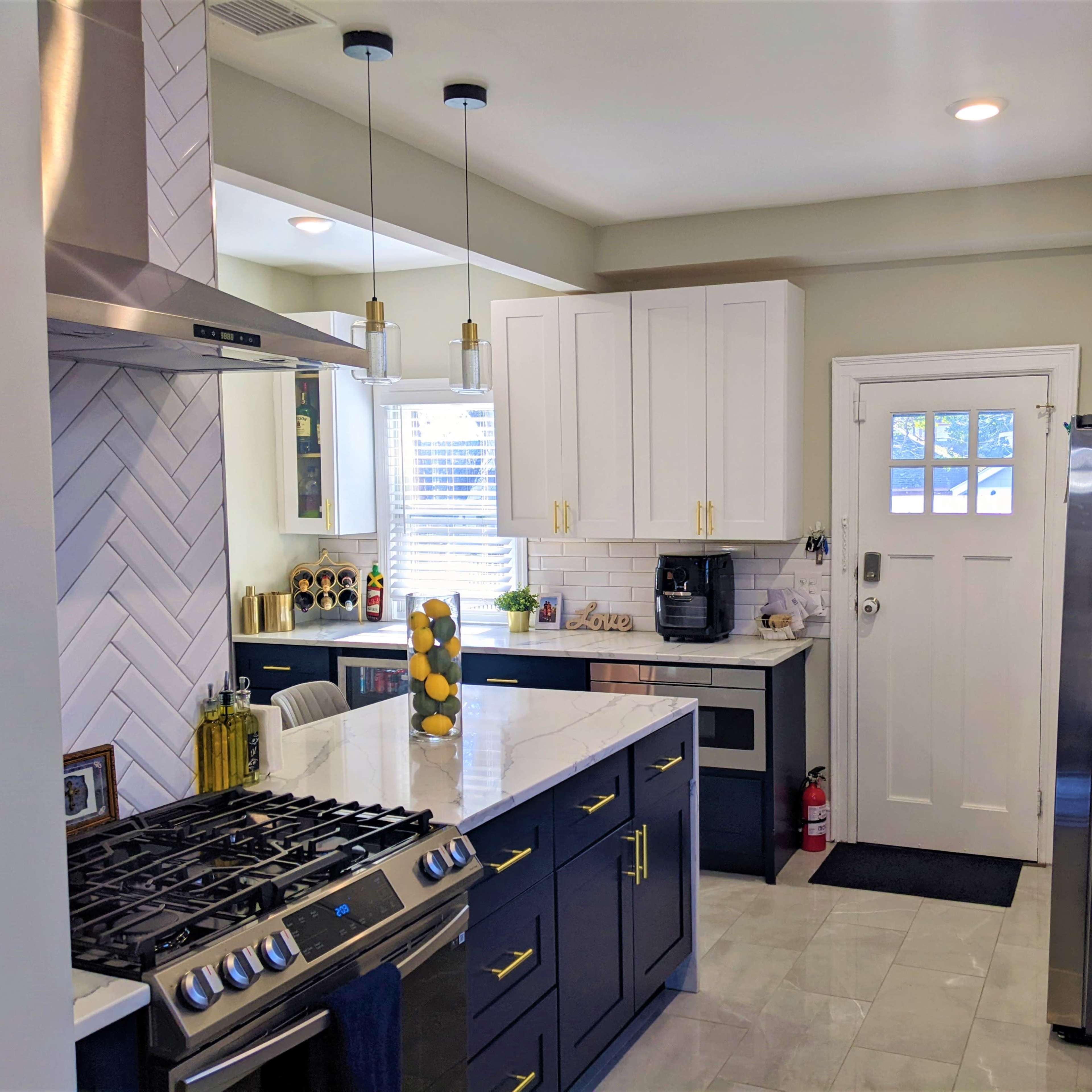 A modern kitchen featuring a marble island, dark blue cabinetry, stainless steel appliances, and a door leading outside.