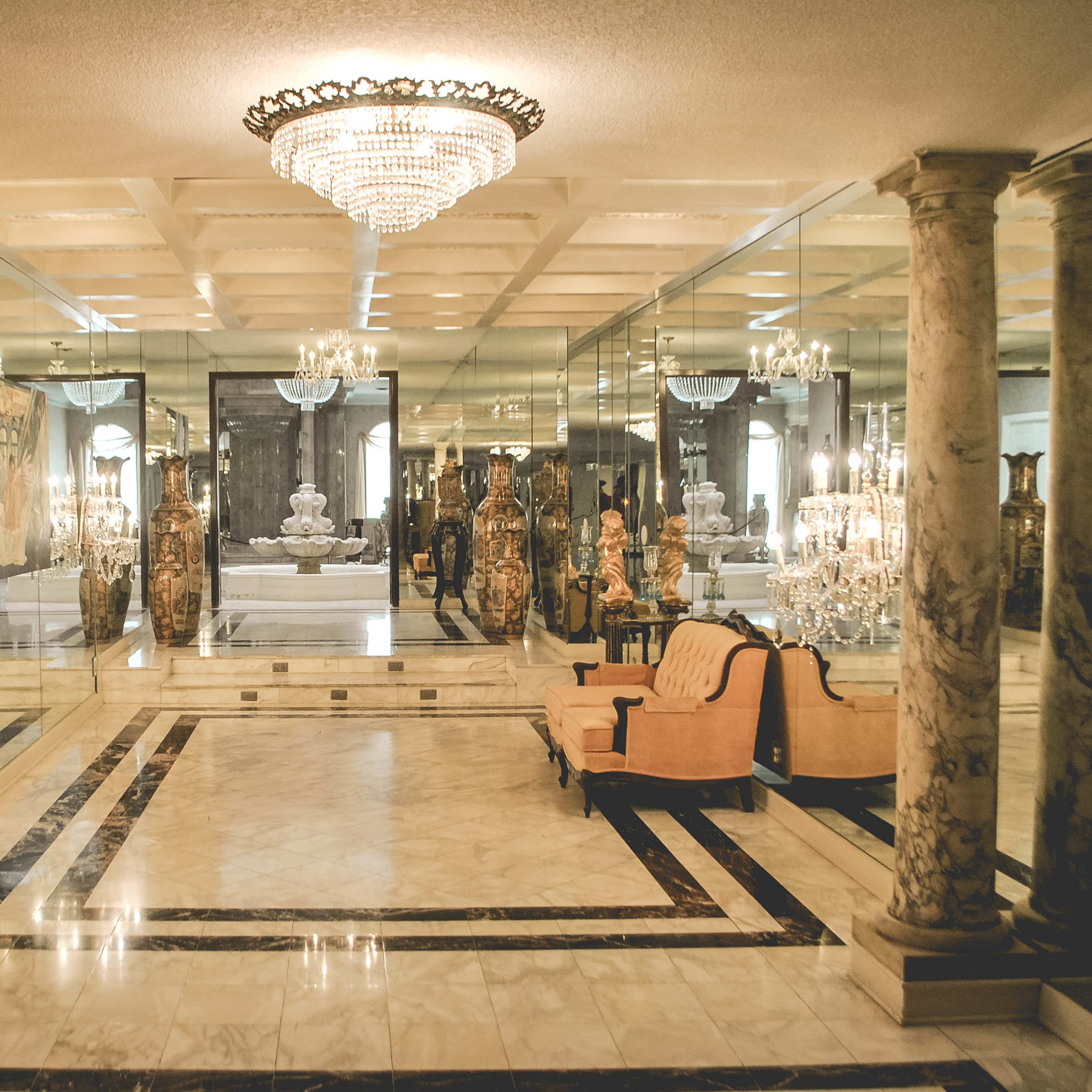 An ornate room featuring marble columns, a chandelier, and elaborate decorations, with a sofa set against mirrored walls.