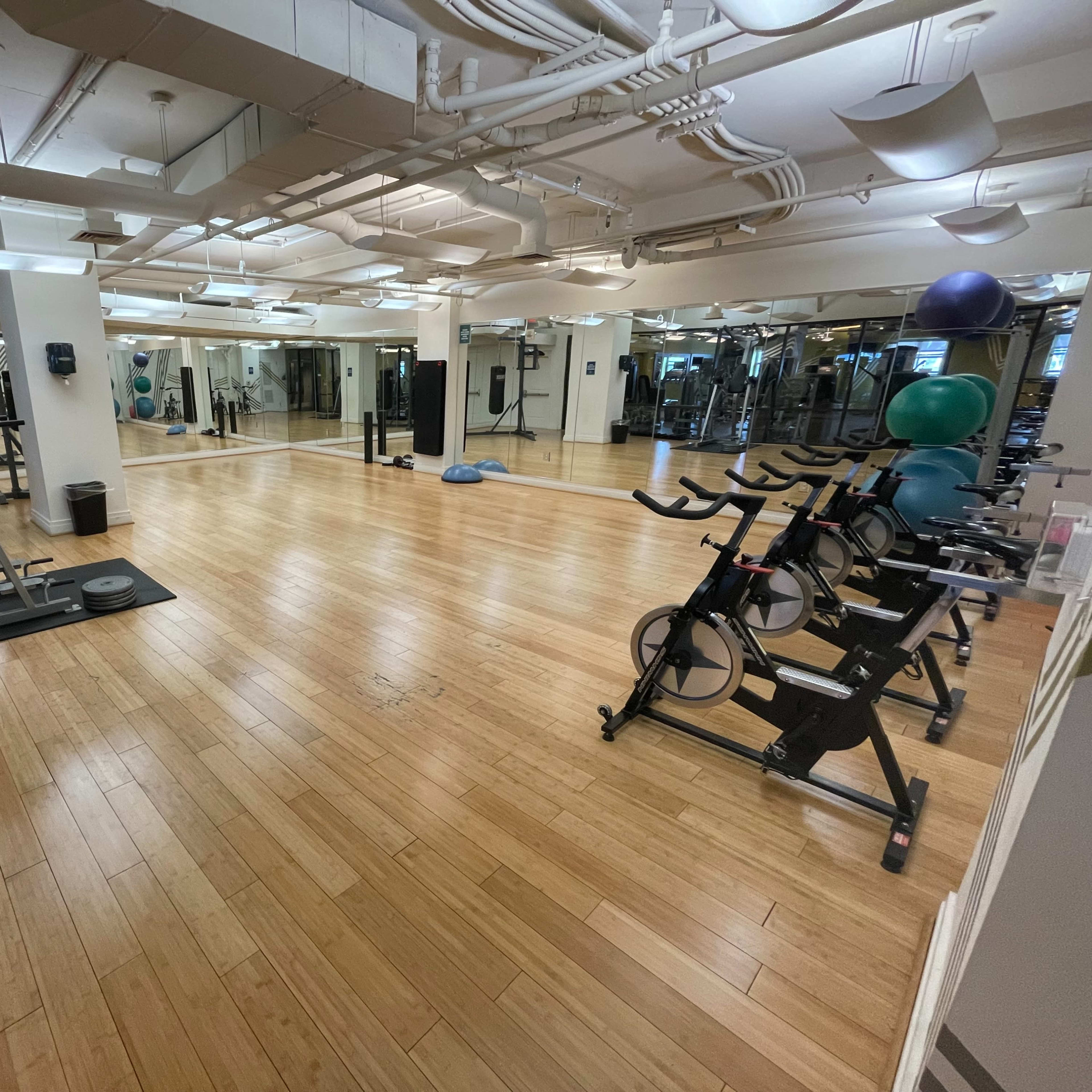 A spacious, well-lit gym with exercise equipment, including stationary bikes and a treadmill, situated on a wooden floor.