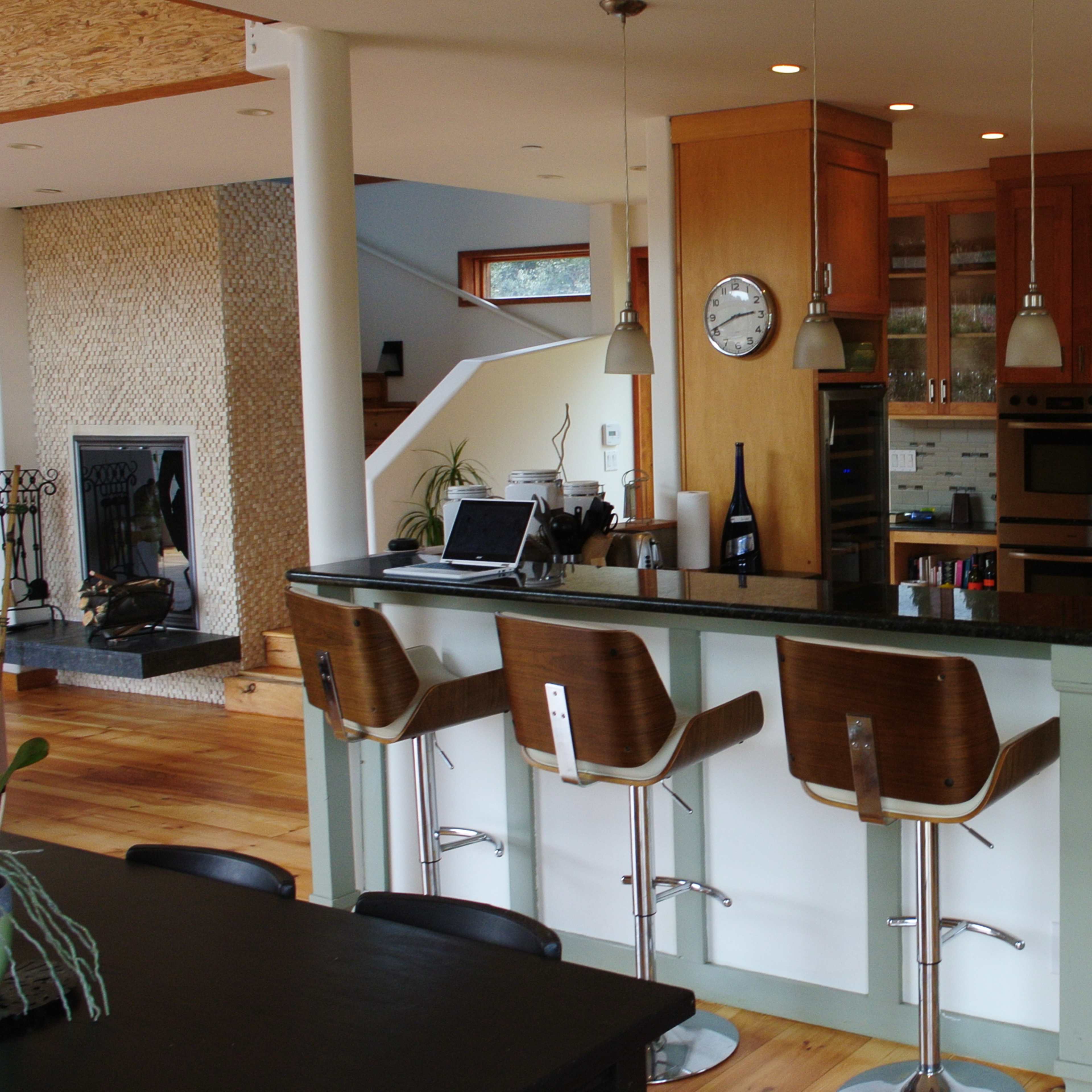 A modern kitchen with wooden cabinets, a large island with bar stools, and a view of a living area in the background.