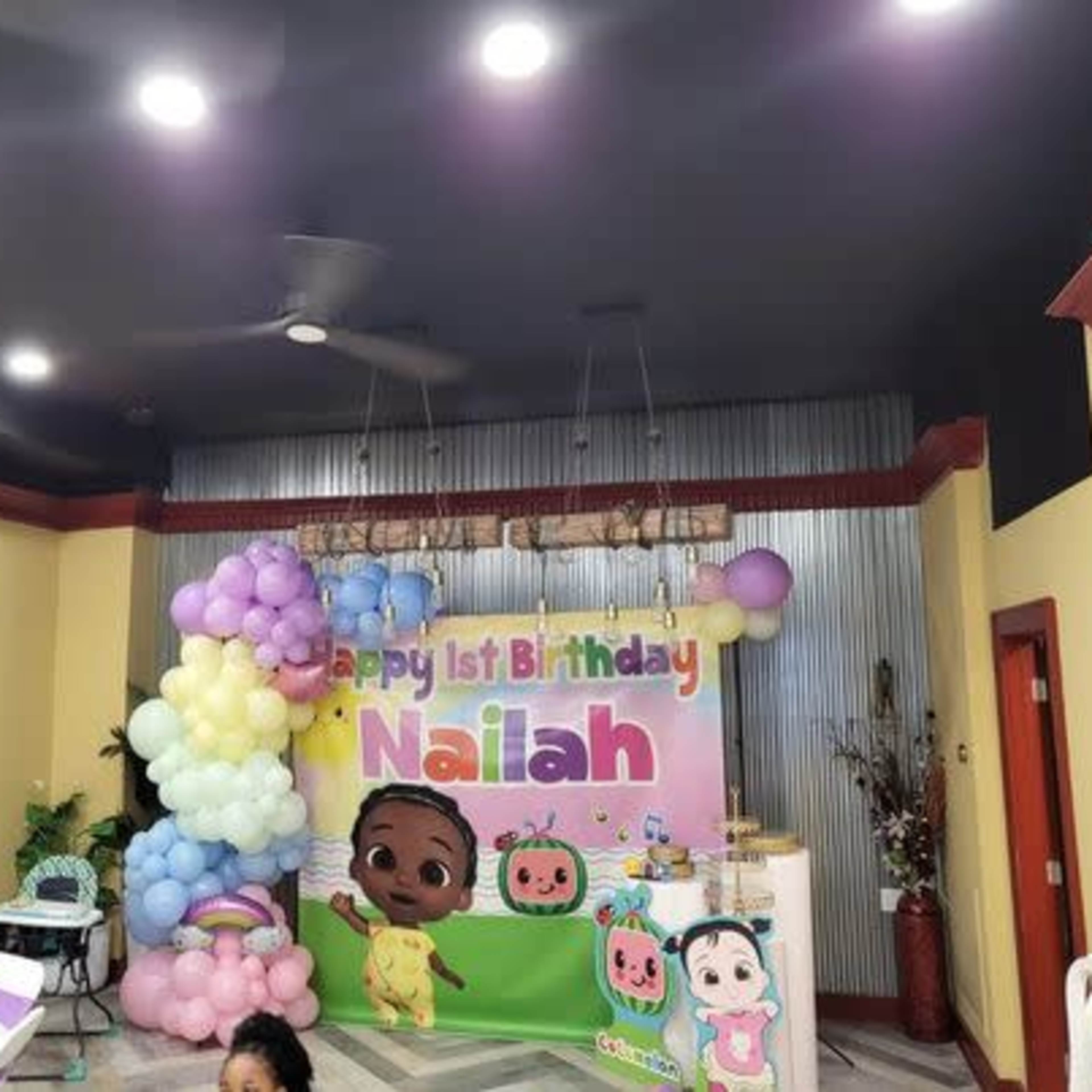 A decorated birthday party scene with a banner reading "Happy 1st Birthday Nailah" and colorful balloons.