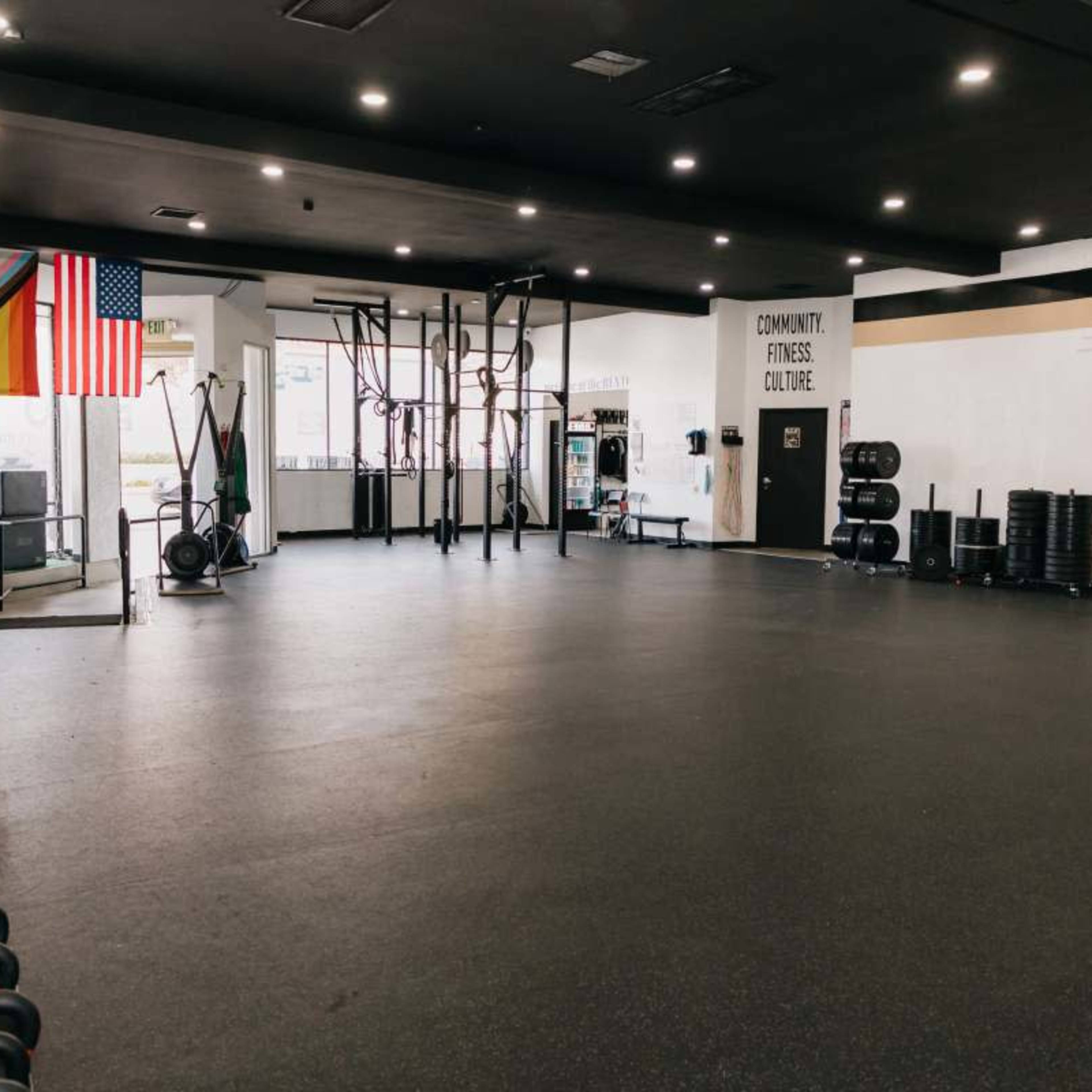 A spacious gym with exercise equipment on the left, large open floor space in the center, and various flags displayed on the walls.