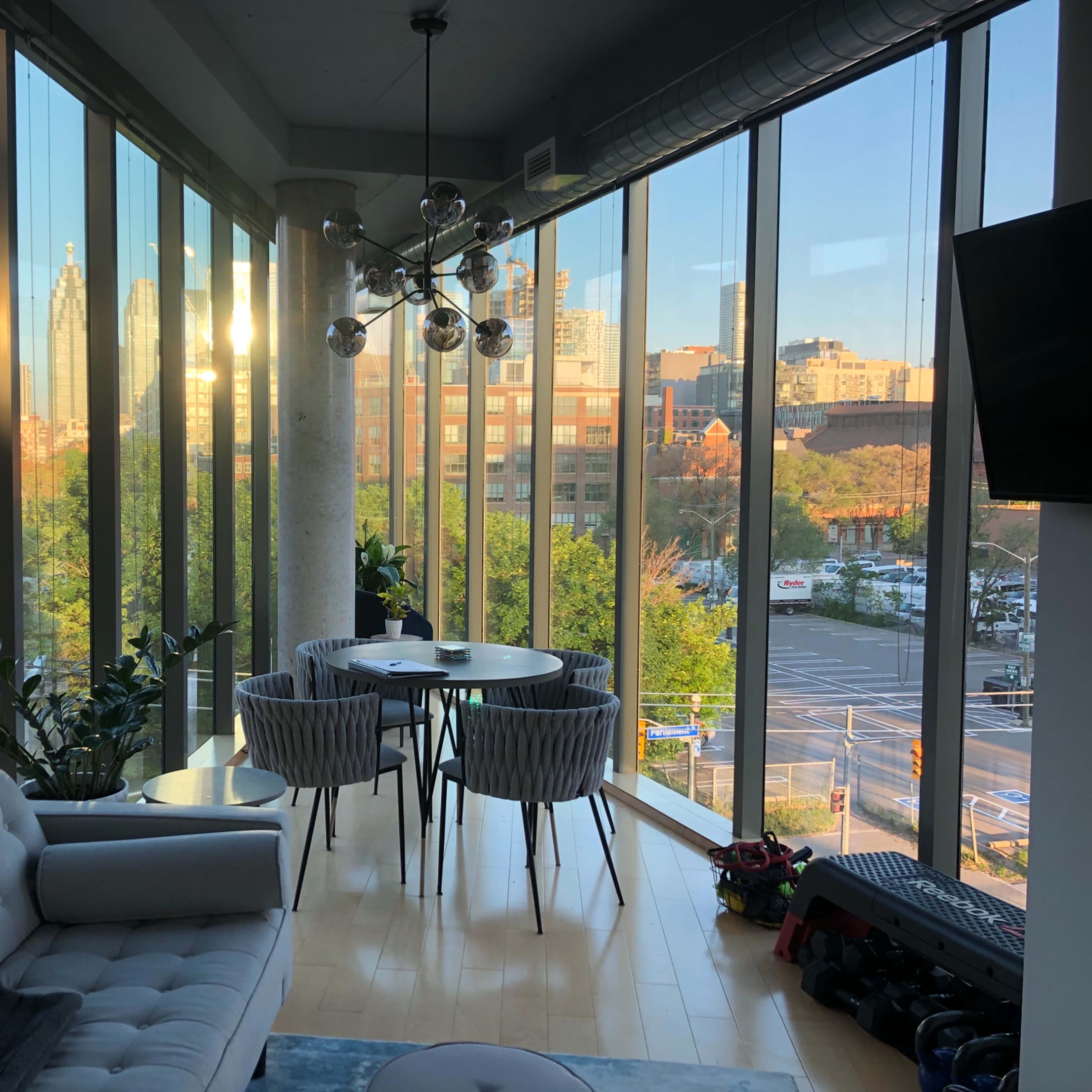 A modern living space features a sitting area with a couch and a dining table surrounded by large windows showcasing a city skyline.