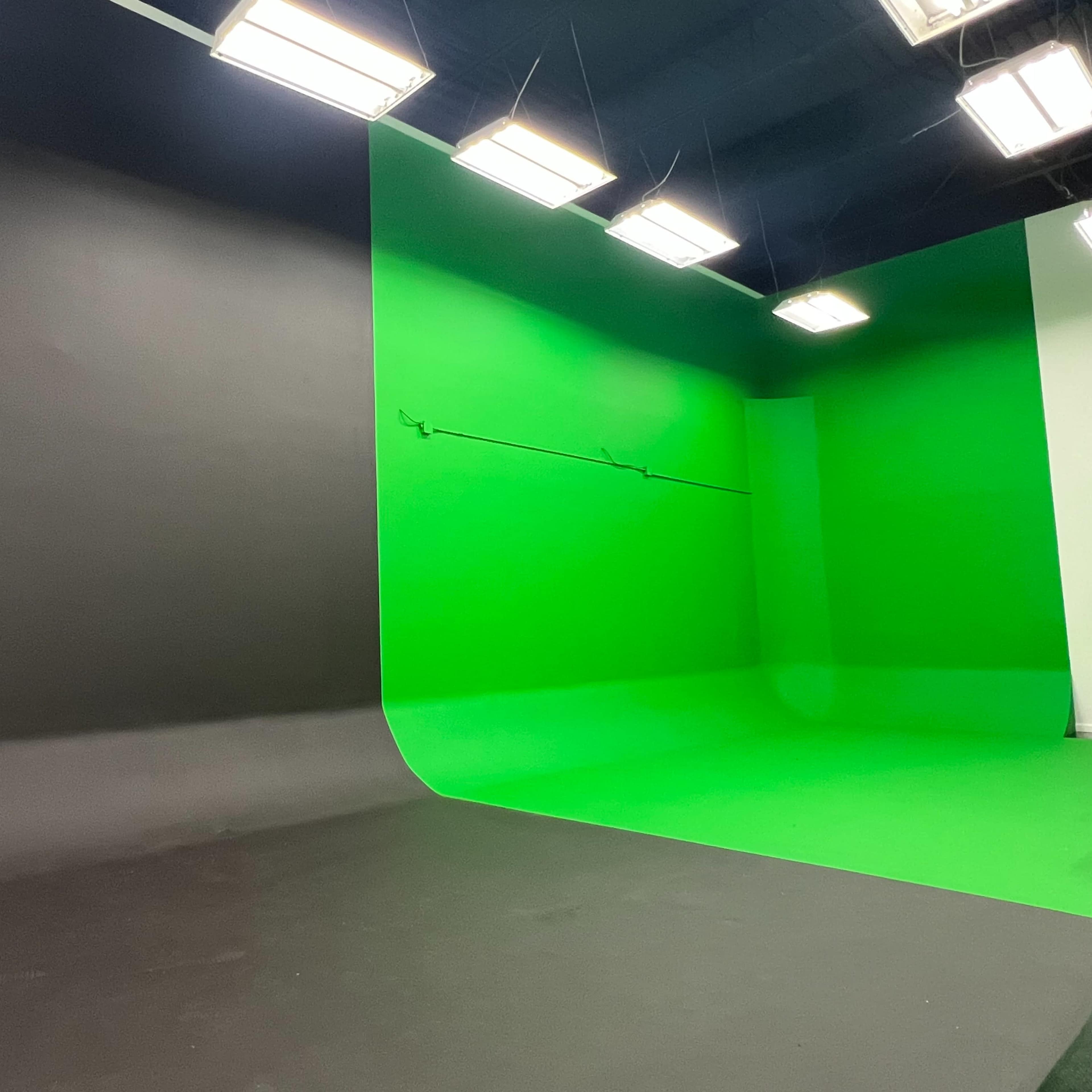 A film studio set with a black backdrop on one side and a green screen backdrop on the other, illuminated by overhead lights.