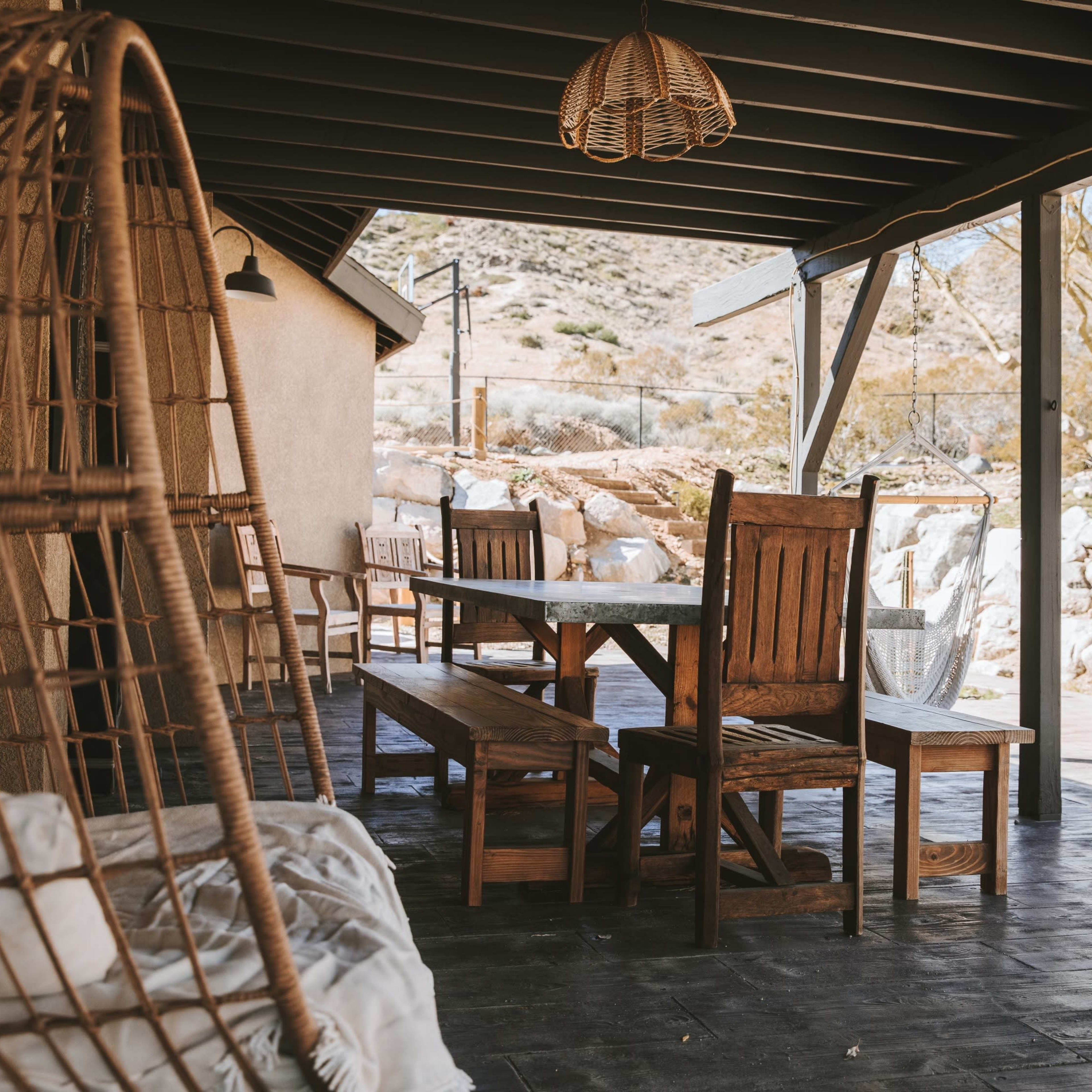 A wooden dining set with benches is placed on a covered patio overlooking a rocky landscape.