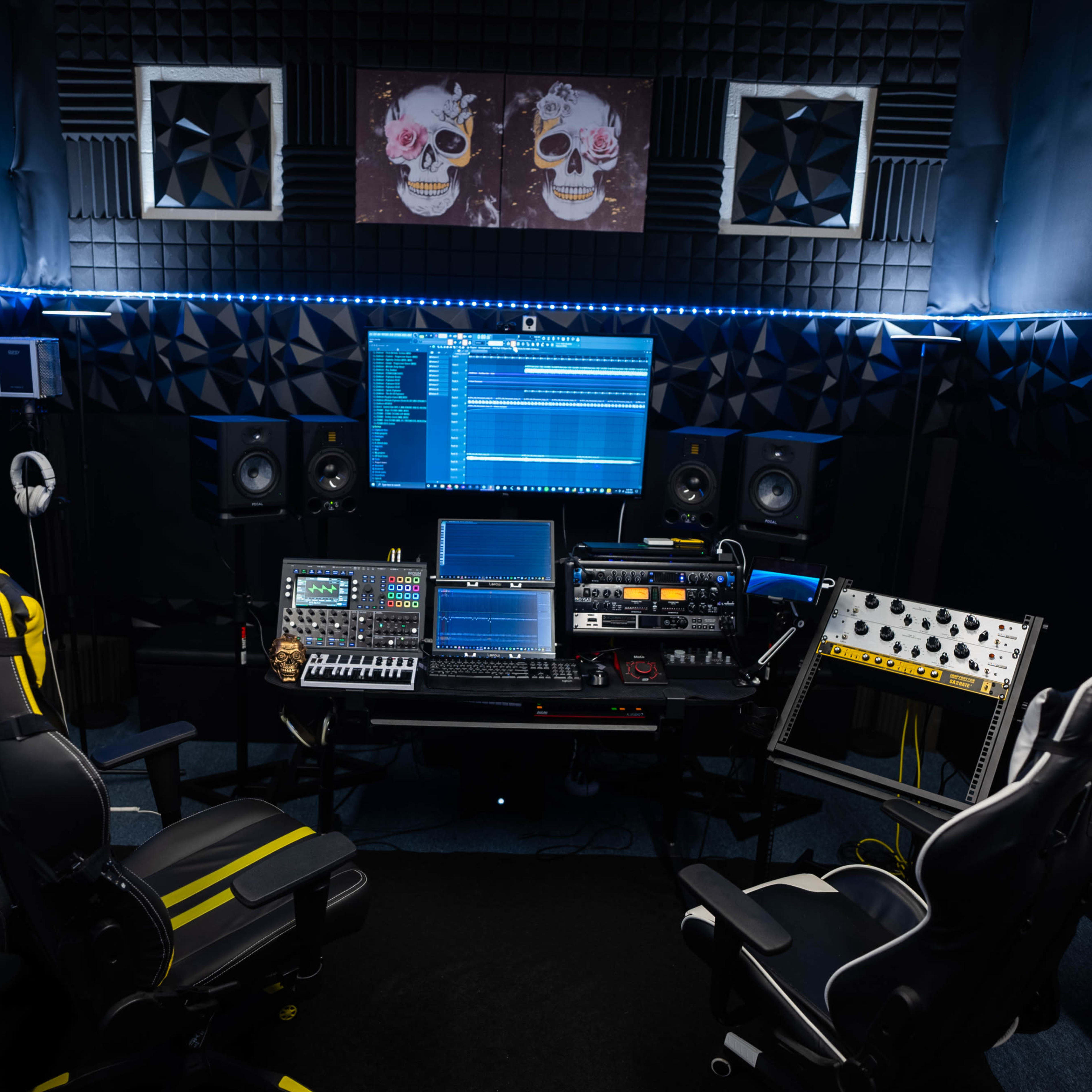 A music production studio with two chairs, multiple monitors, audio equipment, and soundproof wall panels.